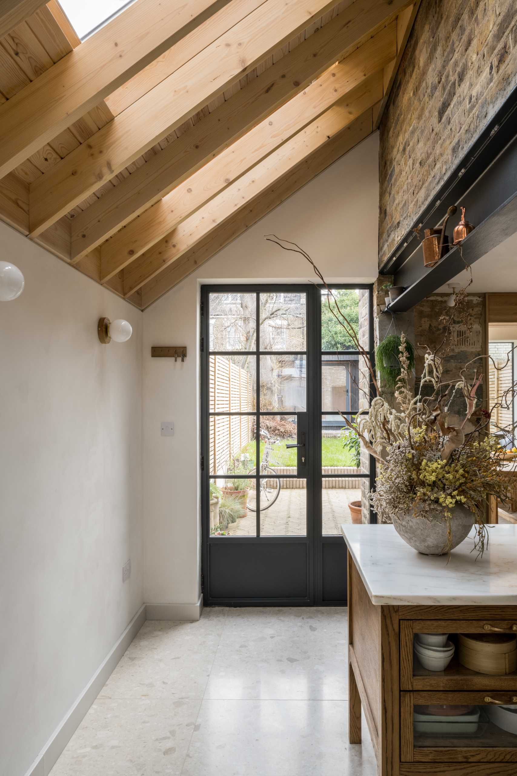 A new extension connects to the rear garden through a black-framed gl، door.