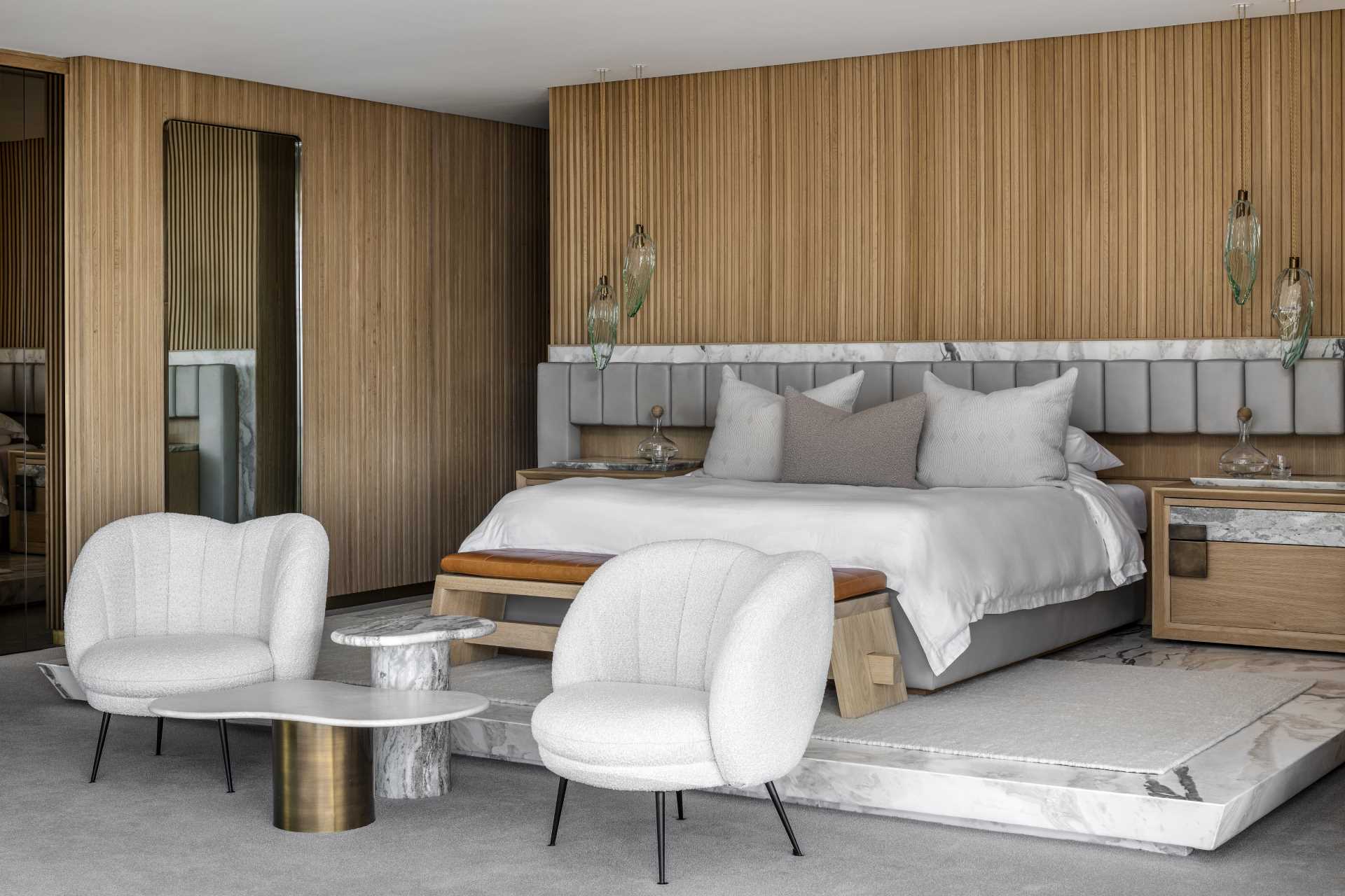 This main bedroom suite has wood walls, a bed that's elevated on a marble platform, and a headboard that spans the width of the bed and the bedside tables.