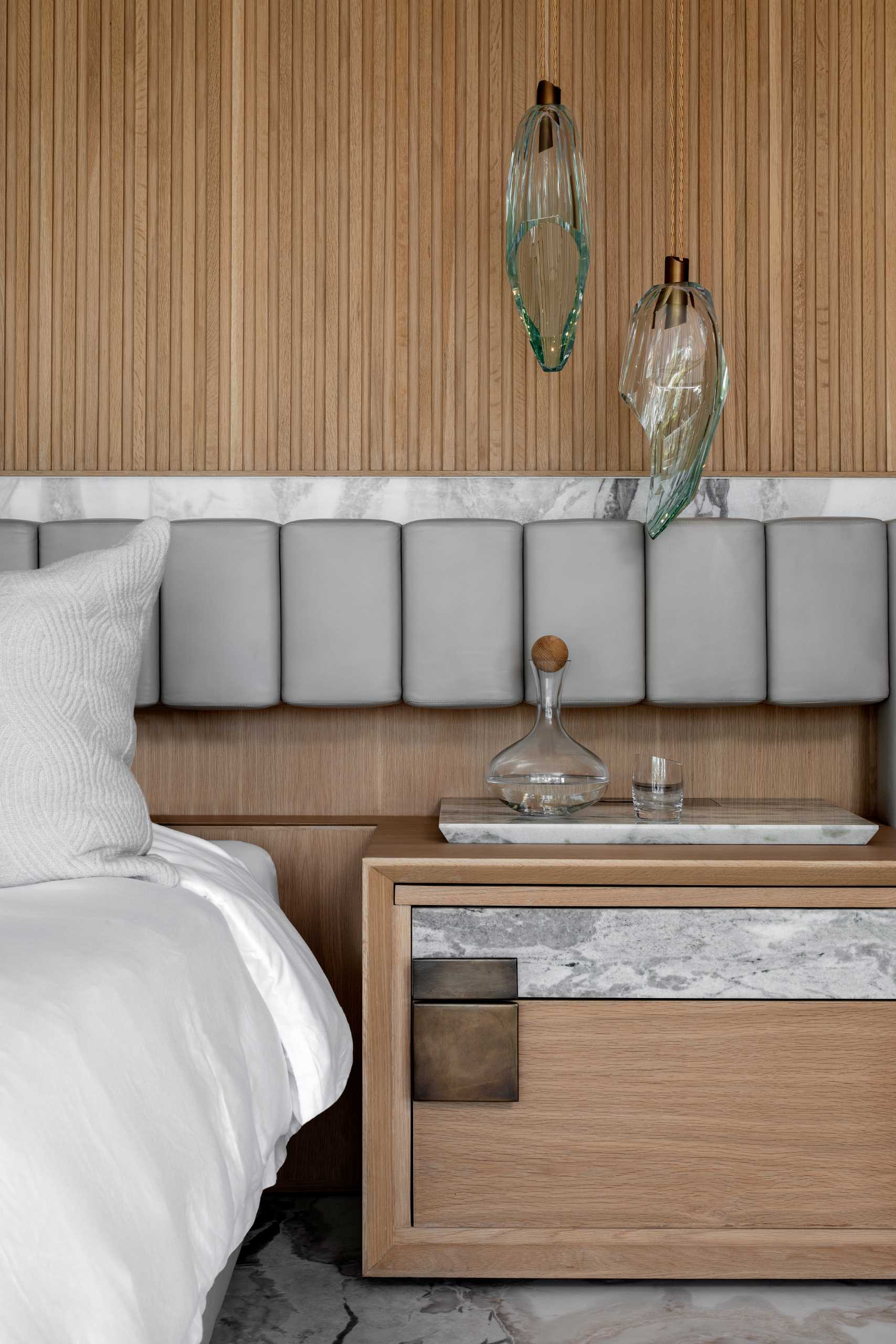 This main bedroom suite has wood walls, a bed that's elevated on a marble platform, and a headboard that spans the width of the bed and the bedside tables.