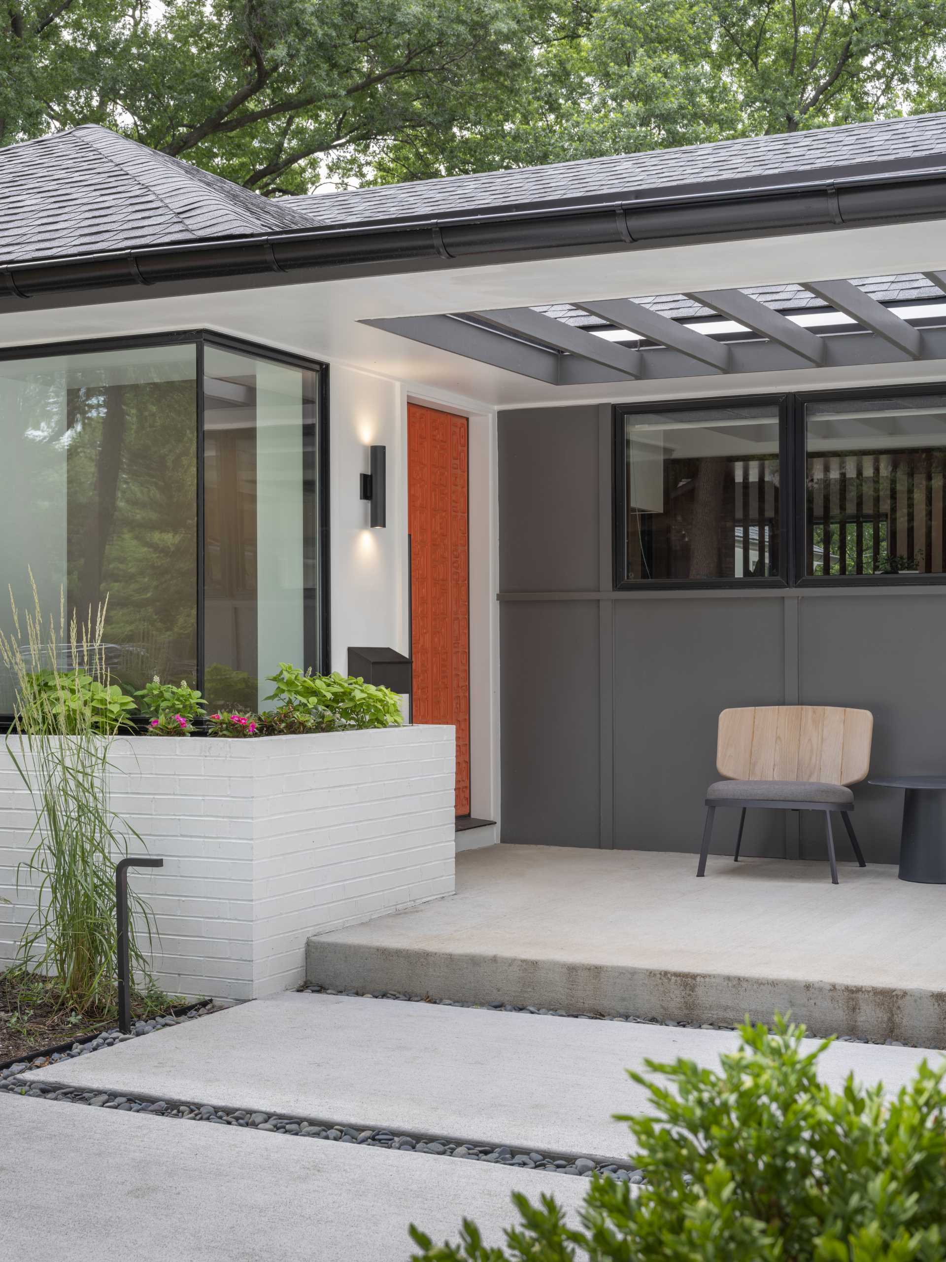 A colorful front door adds brightness to the home and stands out against the grey and white exterior, as well as the nearby plants.