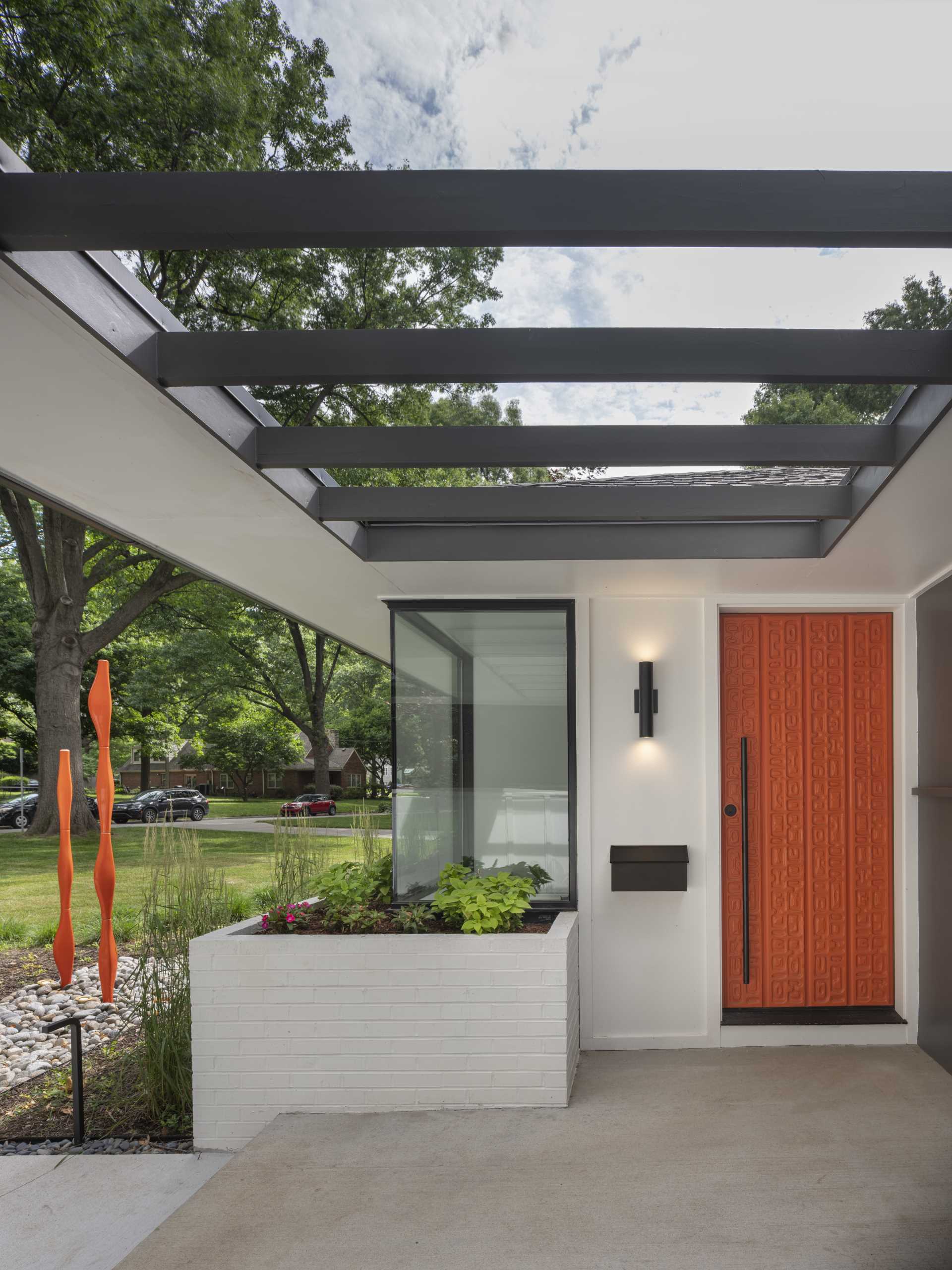 A colorful front door adds brightness to the home and stands out against the grey and white exterior, as well as the nearby plants.