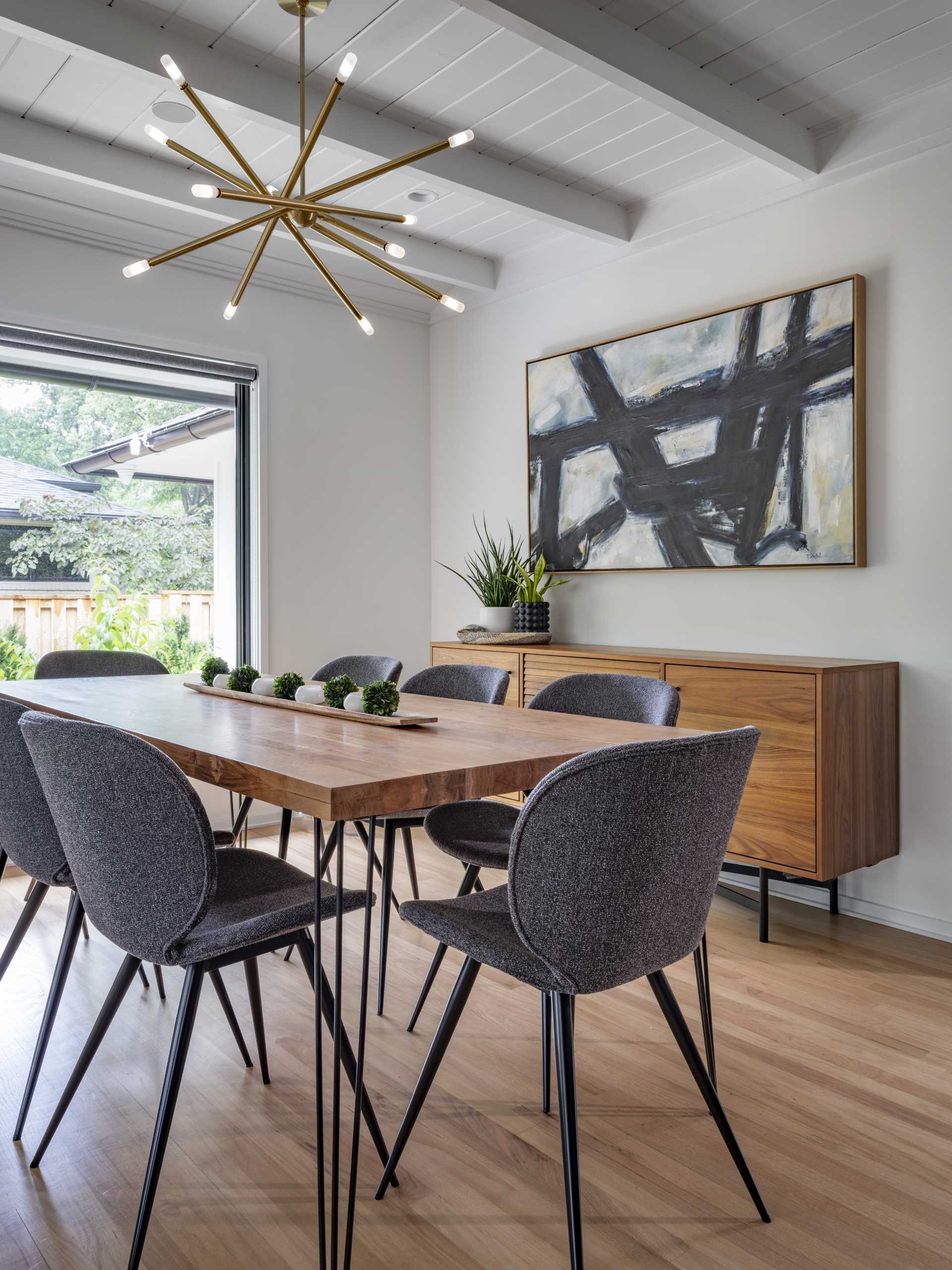 In the dining room, a wood dining table is surrounded by grey upholstered chairs with black legs that match the table design.