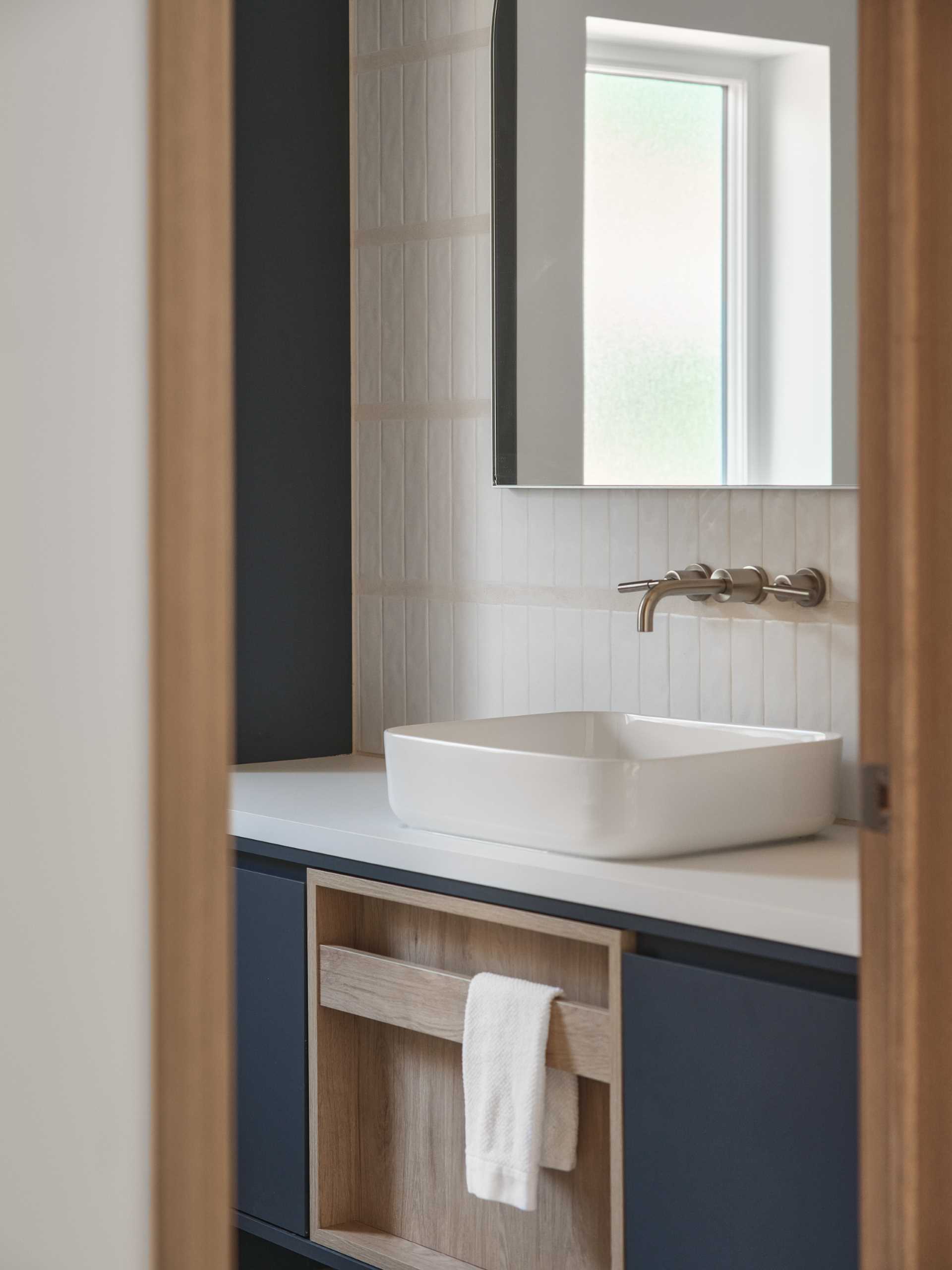 In this modern bathroom, a dark vanity matches the dark wall, while white tiles provide a backdrop for the mirror.