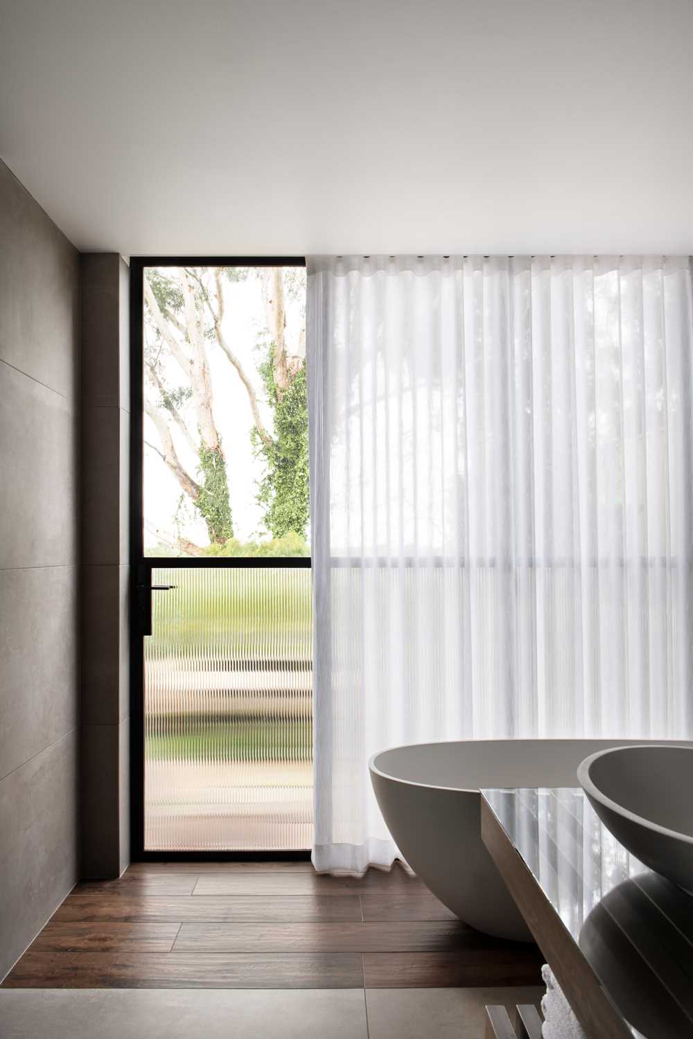 The black-framed steel glass doors connect to the completely private garden, while the soft curtain creates a softness for the bathroom.
