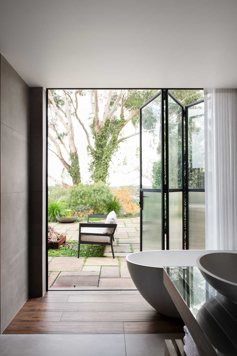 The black-framed steel glass doors connect to the completely private garden, while the soft curtain creates a softness for the bathroom.
