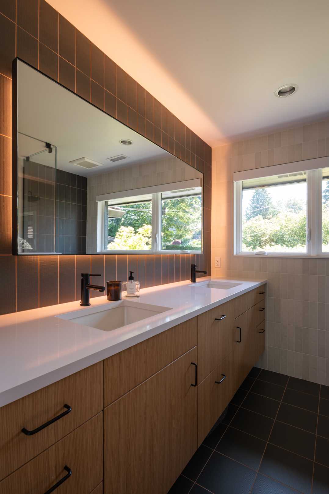 The updated primary bathroom received a changed layout, with the new double vanity located on the left wall, and the shower and toilet now located on the right. A glass shower screen allows the natural light from the window to flow through the space. Additional light has been added to the bathroom in the form of hidden LEDs behind the mirror.