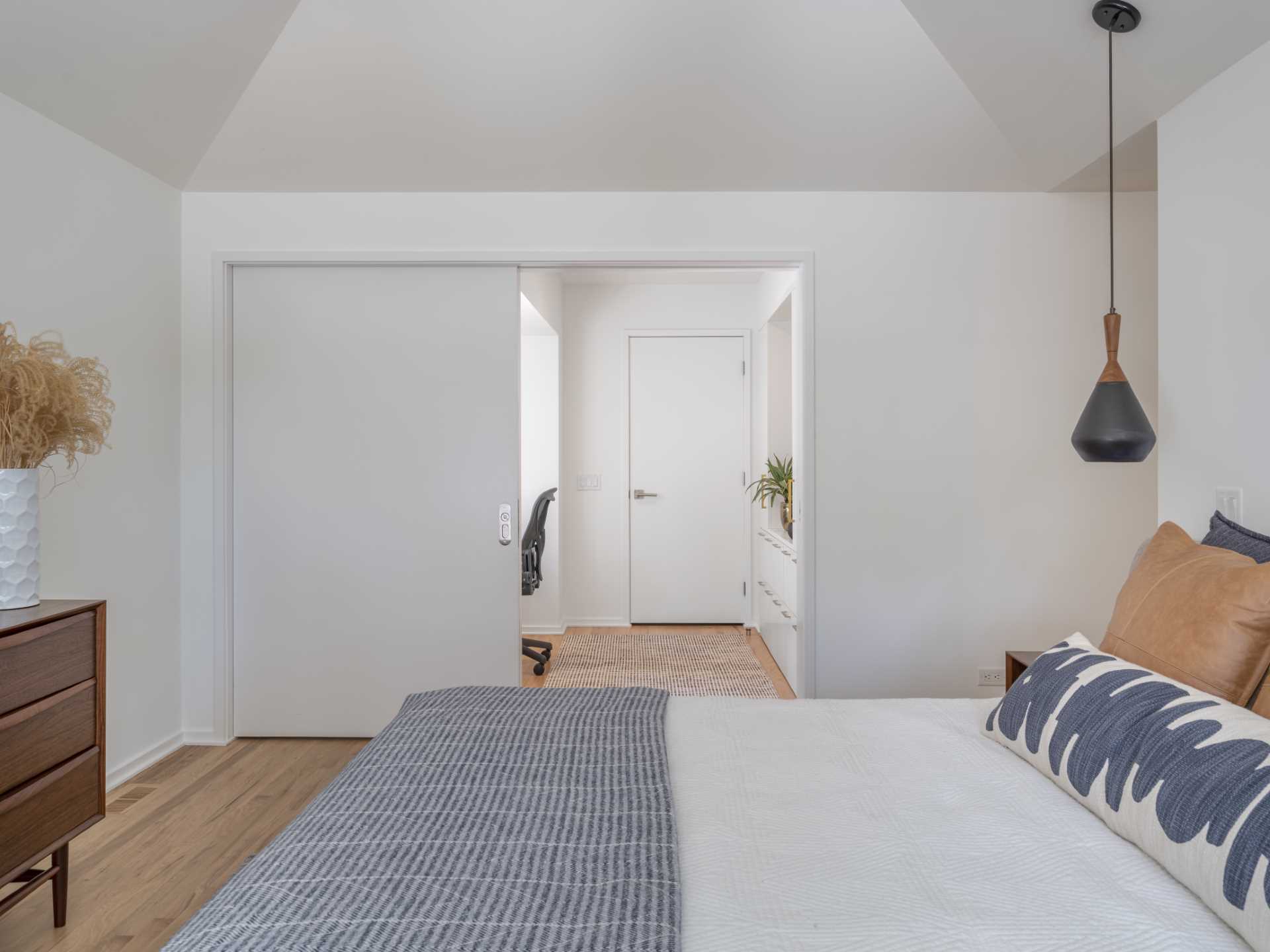 A home office is located behind a sliding door in the bedroom and includes a built-in wood desk and a wall of storage.