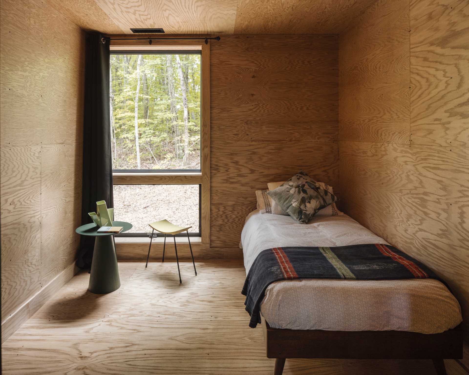 A bedroom lined with wood include a vertical window for natural light and views of the trees.