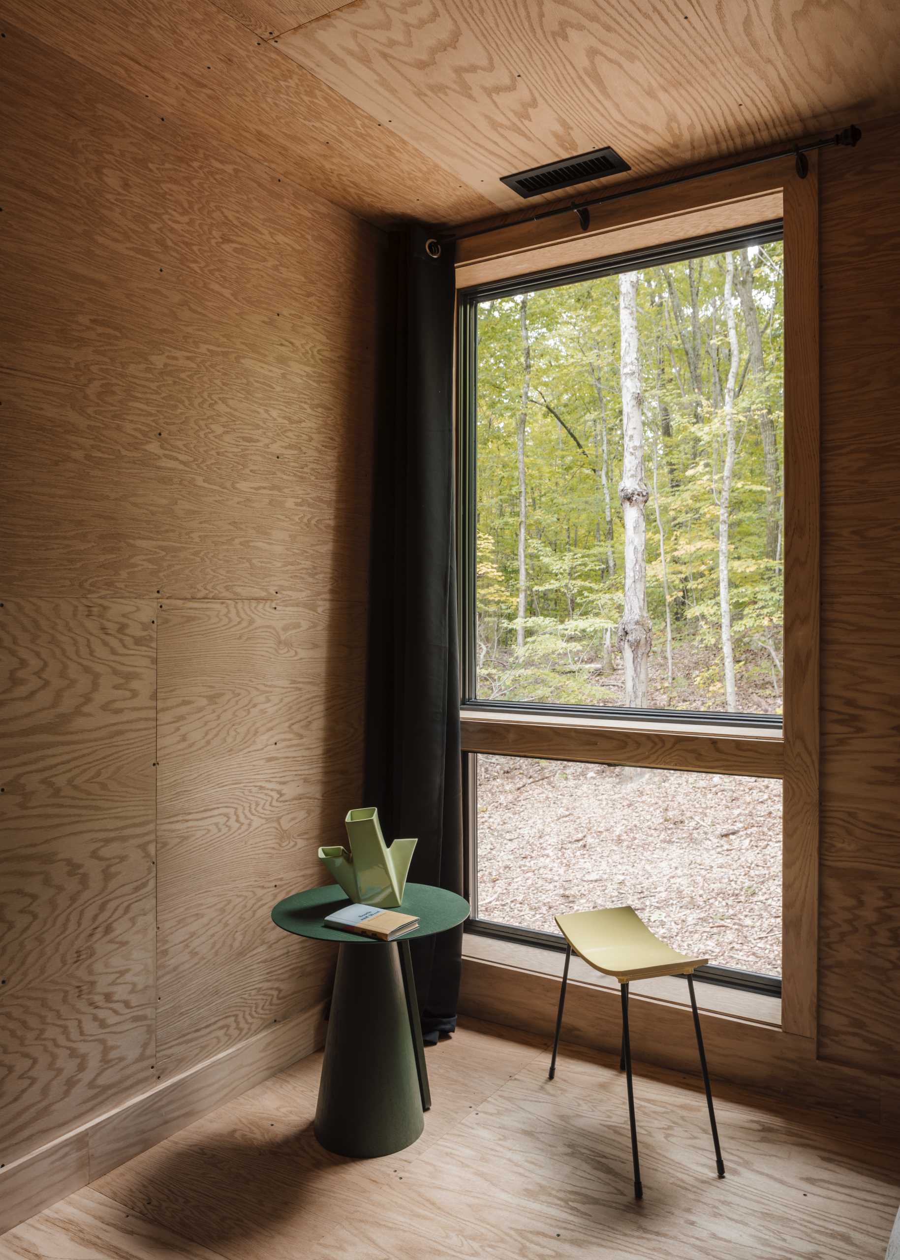 A bedroom lined with wood include a vertical window for natural light and views of the trees.