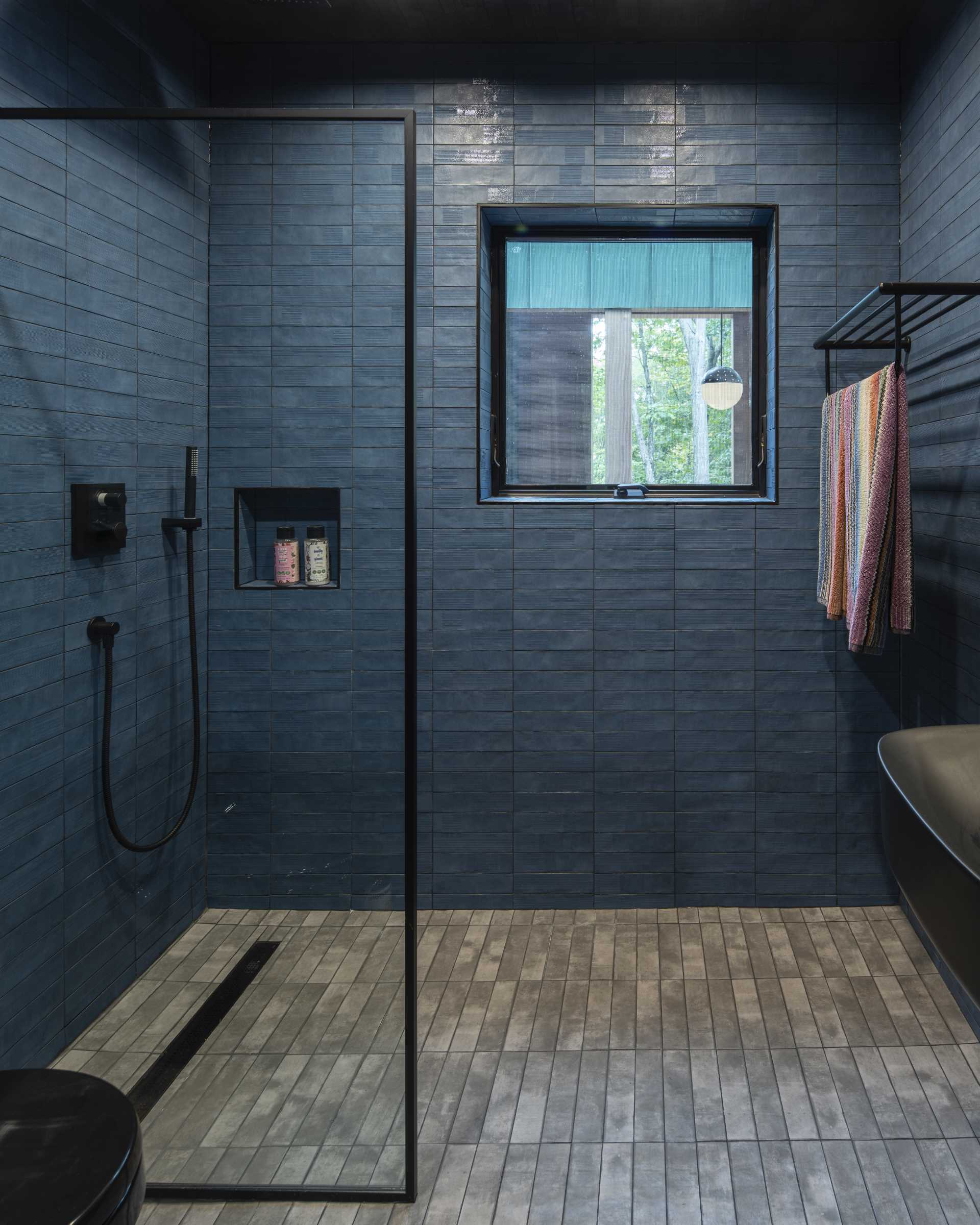 In this modern bathroom, blue tiles line the walls, grey tiles line the floor, and accents of black provide a contrasting element.