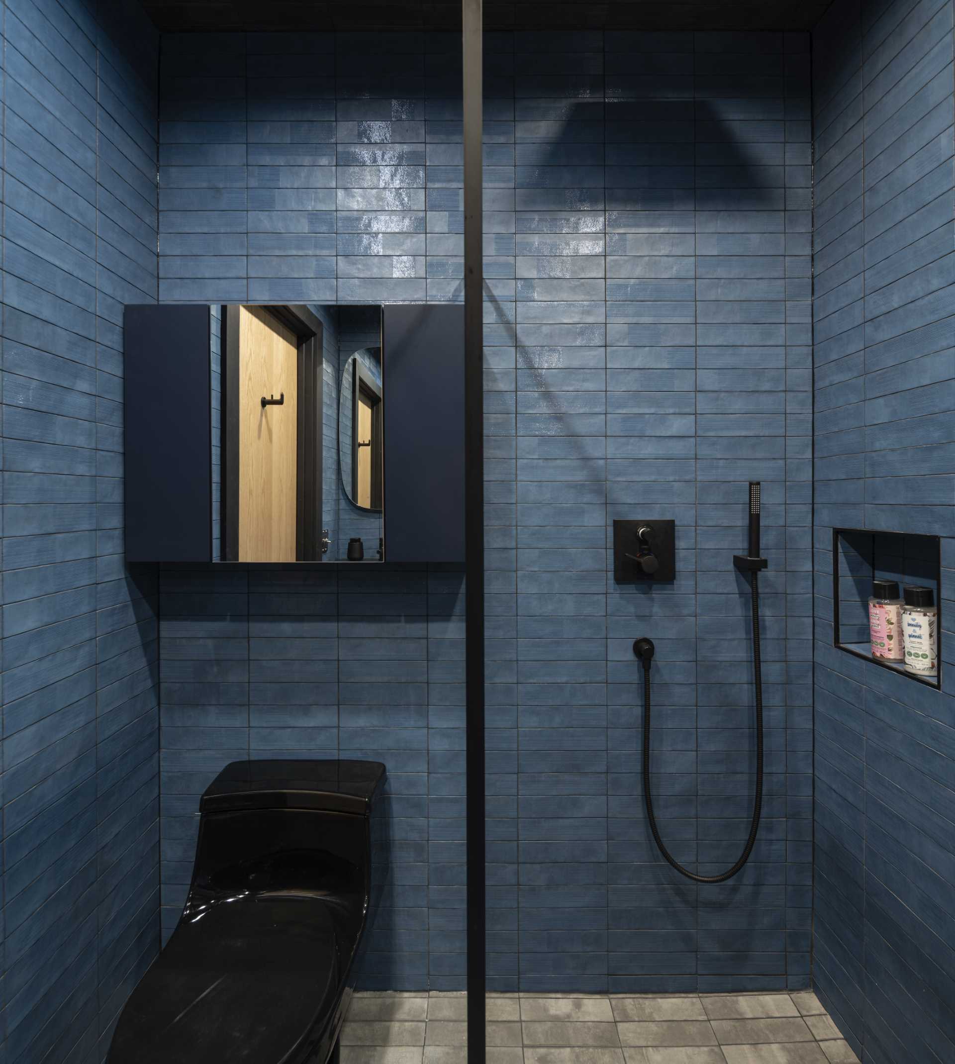In this modern bathroom, blue tiles line the walls, grey tiles line the floor, and accents of black provide a contrasting element.