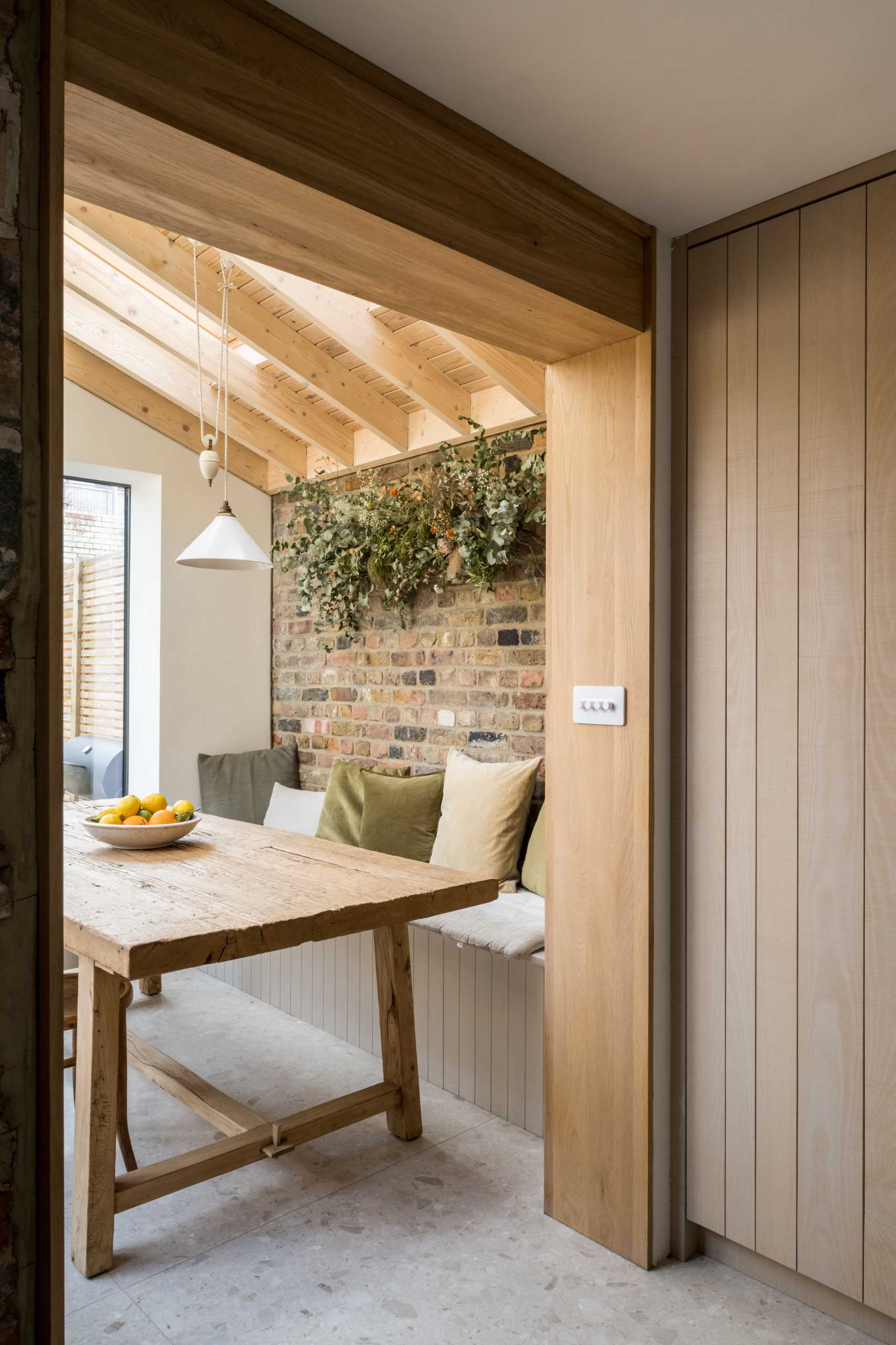 In this dining room, a built-in dining bench creates a cozy corner that provides a comfortable ledge and surrounds a rustic dining table made from reclaimed structural timbers.