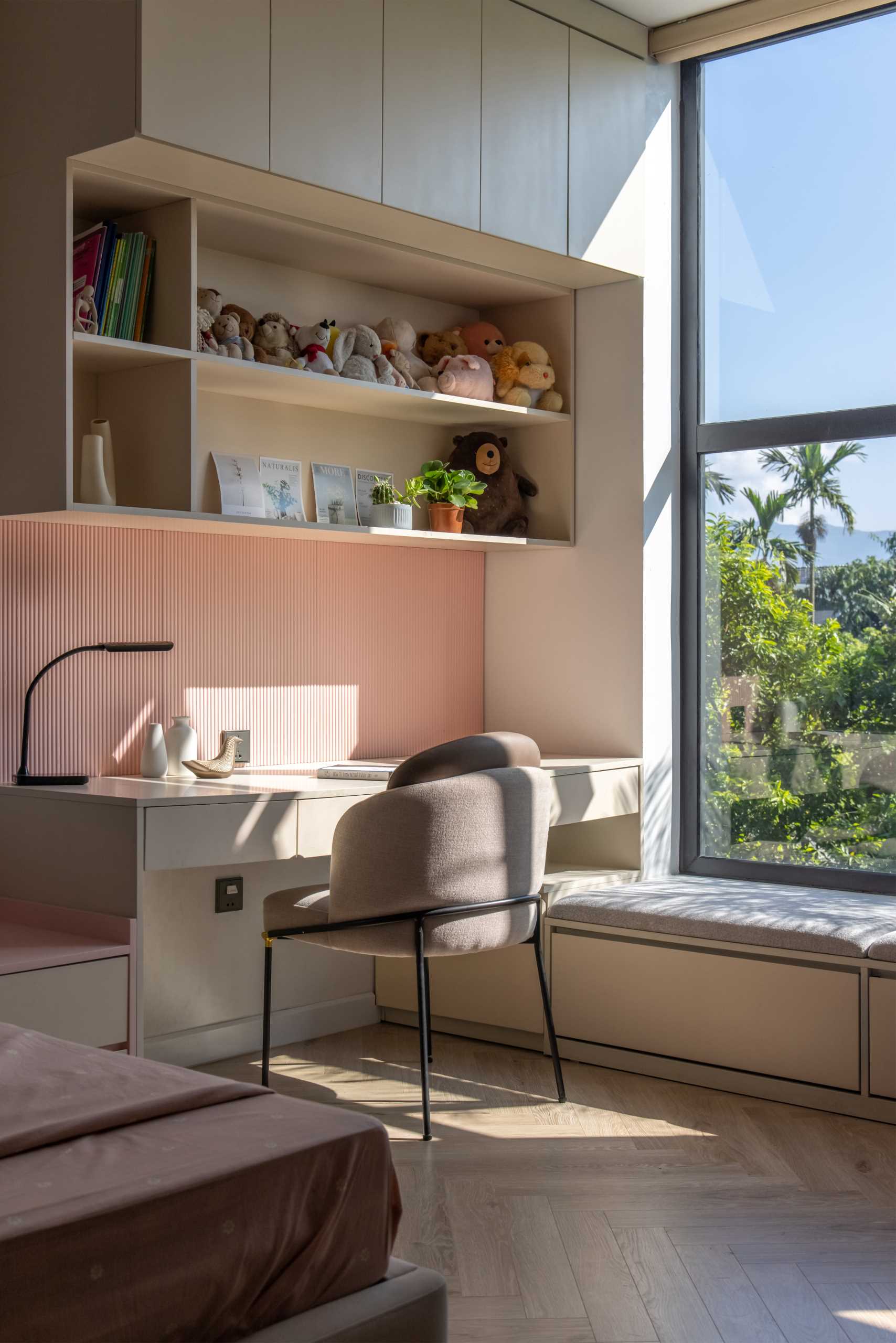 In this kids' bedroom, there's a custom-designed desk with shelving and cabinetry, as well as a bench underneath the window. On the opposite wall, there's the door to the ensuite bathroom and a floor-to-ceiling closet.