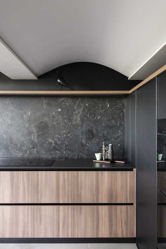 Dark timber doors, Black Dekton benchtops, and an organic black leathered marble splashback are all featured in this modern kitchen design.