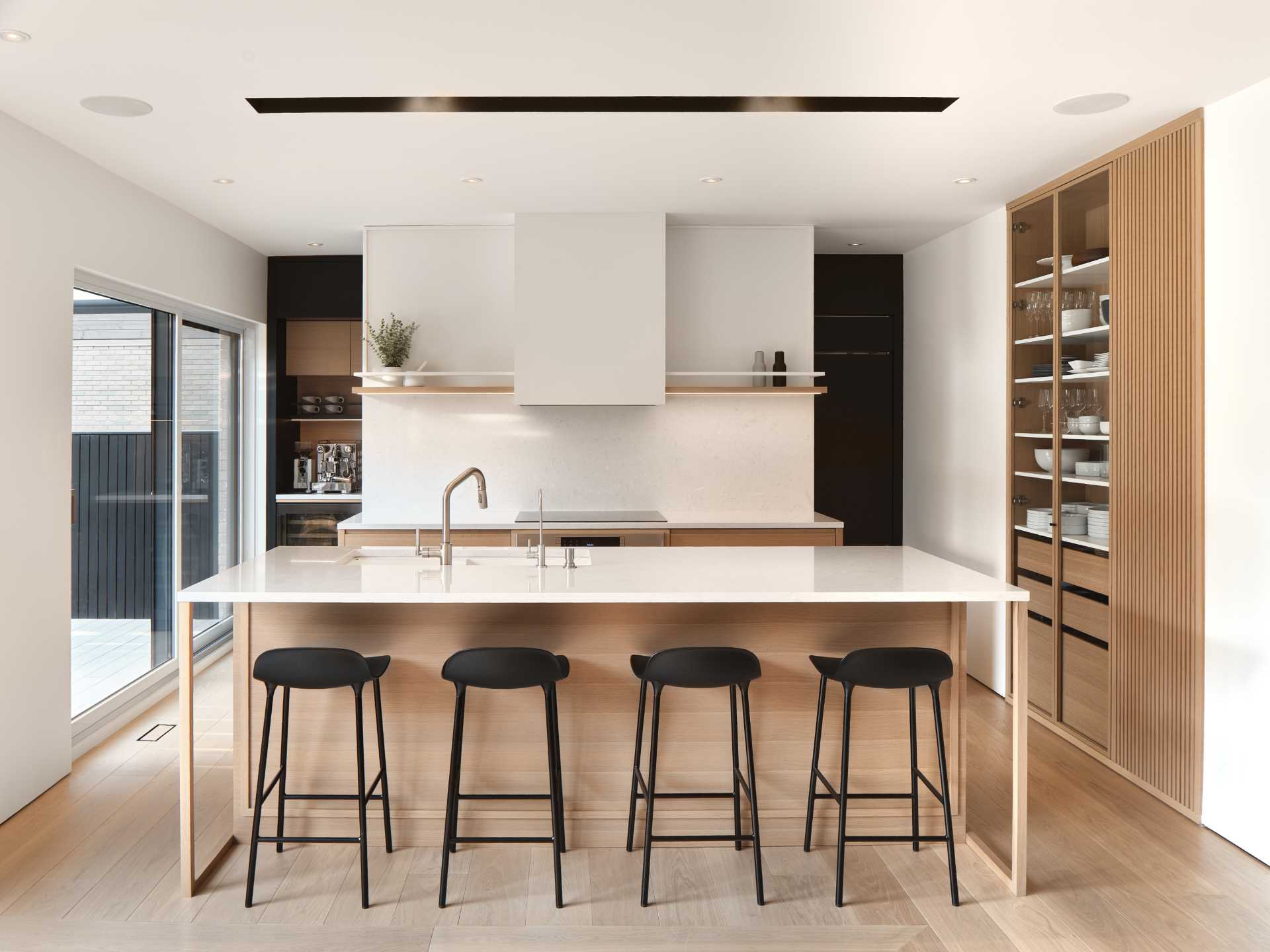 In this modern kitchen, an island creates additional storage and room for seating, while an open shelf built into the wall provides a place to display dinnerware and glassware.