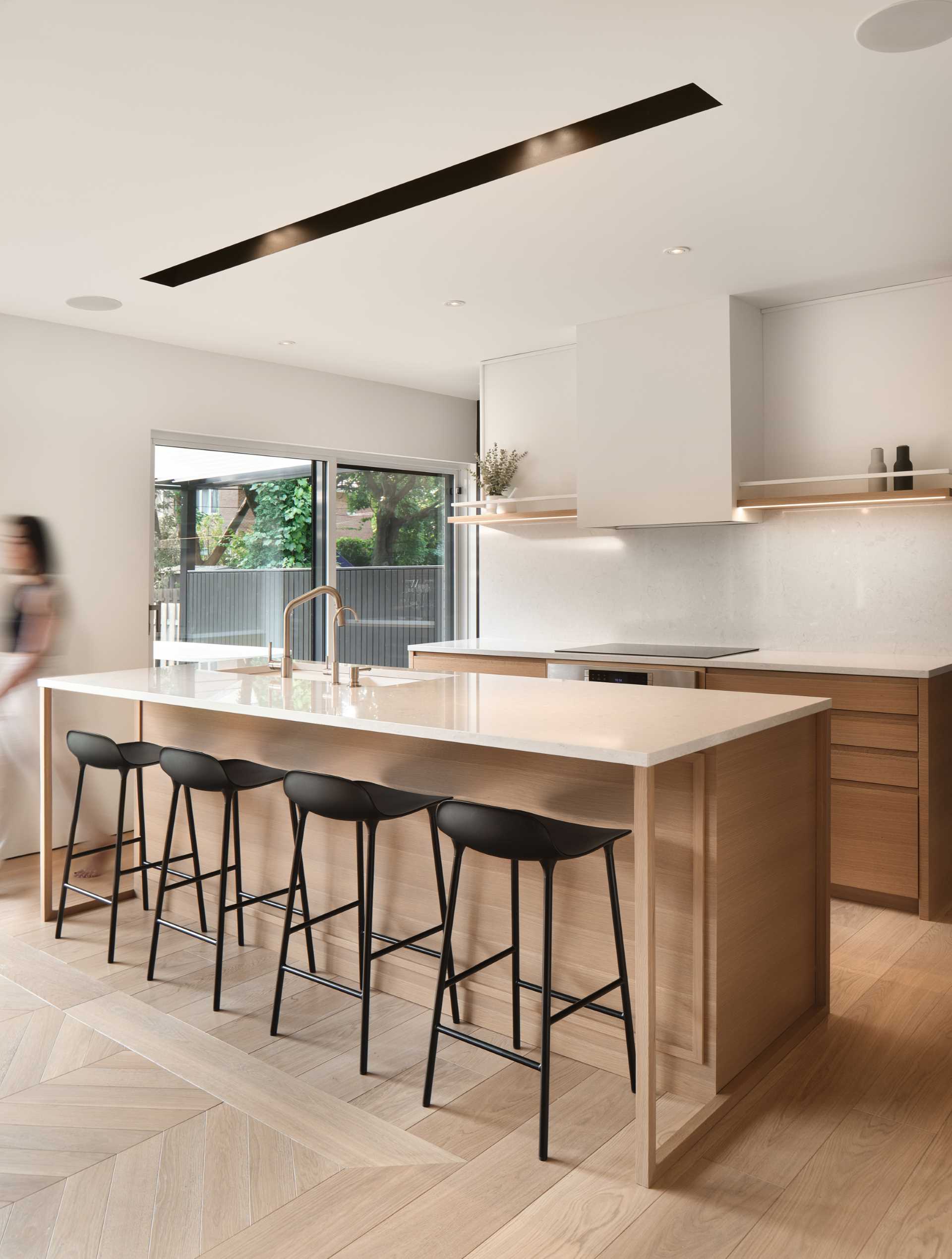 In this modern kitchen, an island creates additional storage and room for seating, while an open shelf built into the wall provides a place to display dinnerware and glassware.