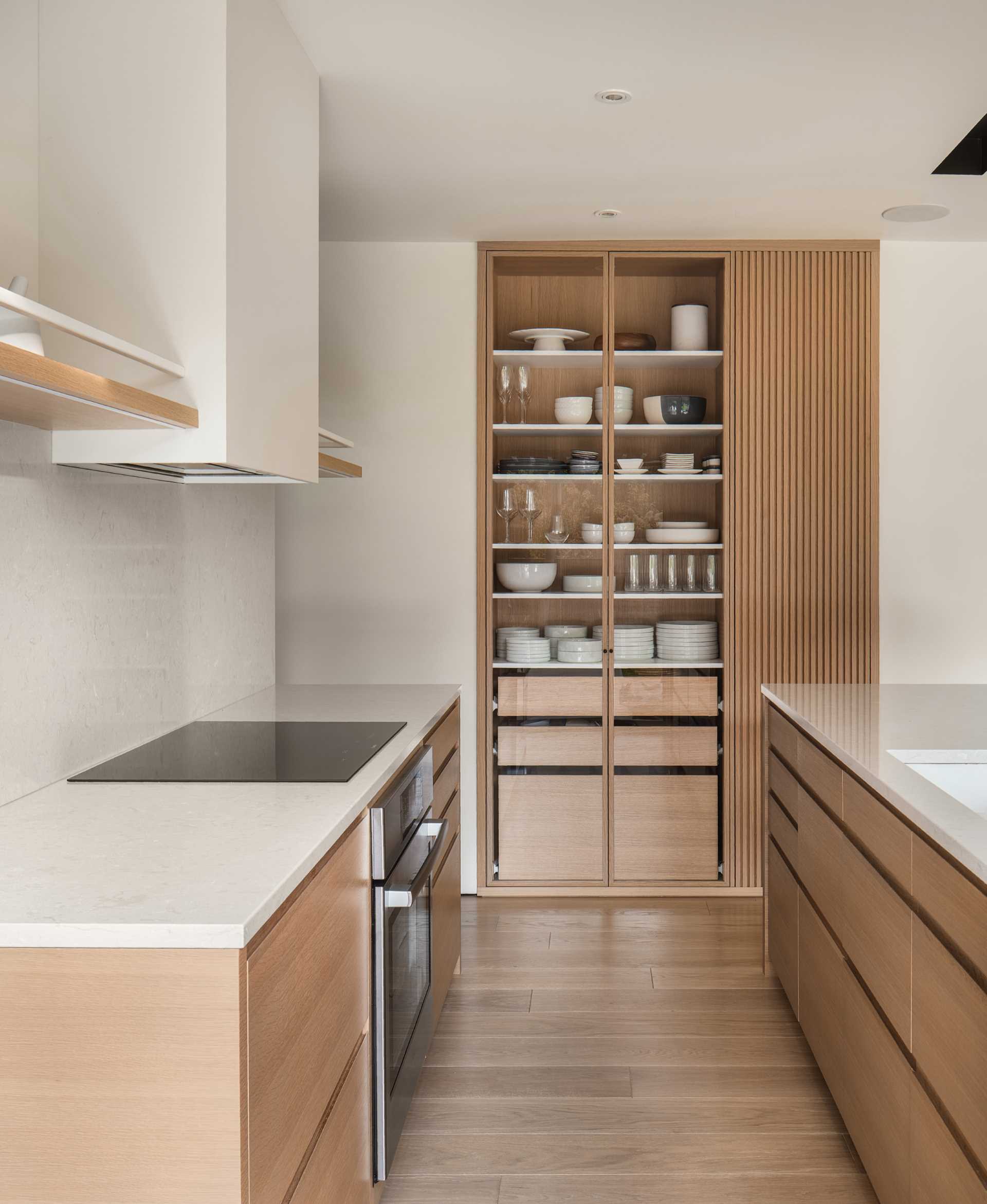 In this modern kitchen, an island creates additional storage and room for seating, while an open shelf built into the wall provides a place to display dinnerware and glassware.