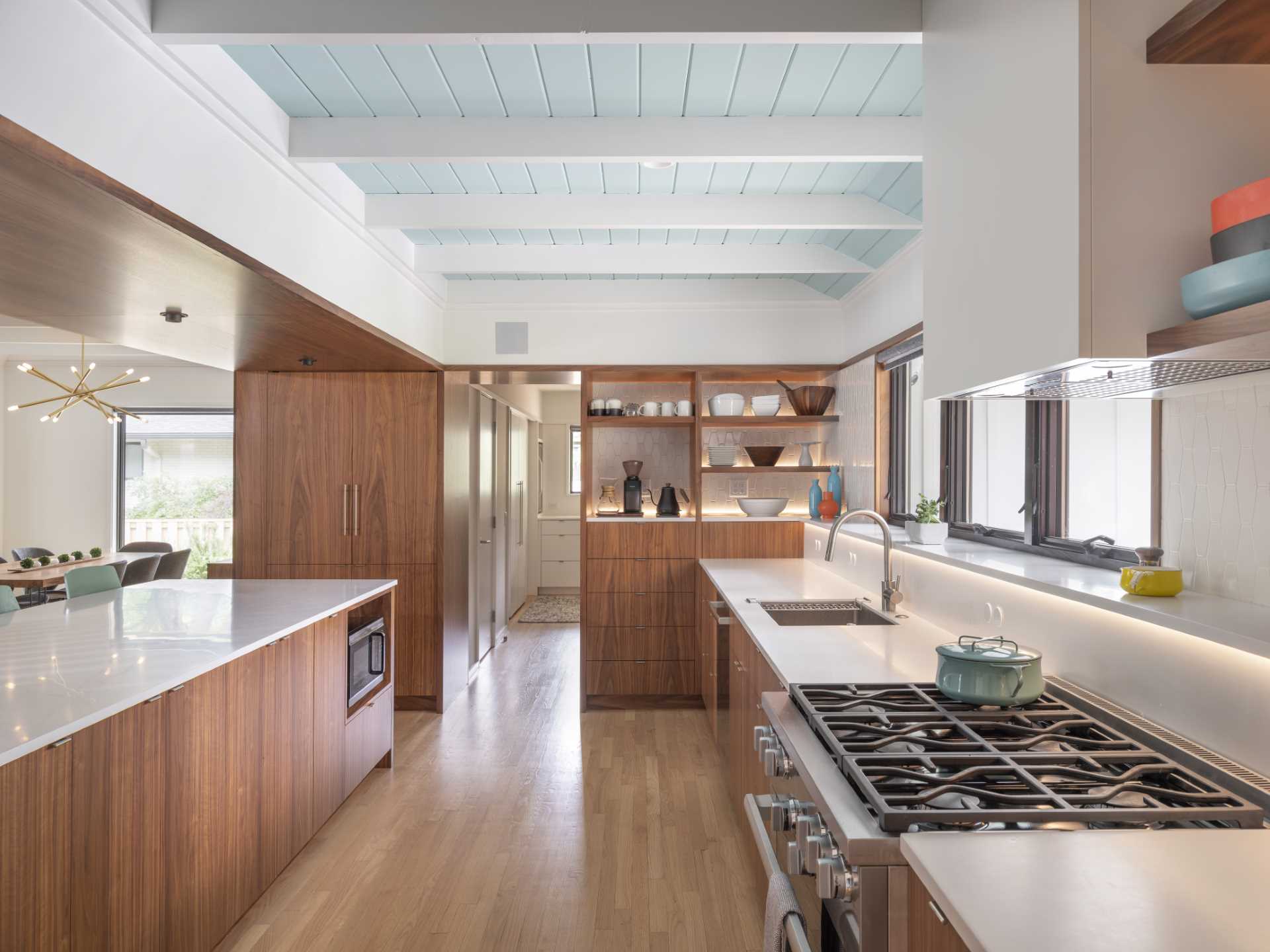 In this updated kitchen, wood cabinetry has been paired with white countertops with matching white tiles, and a light blue ceiling.