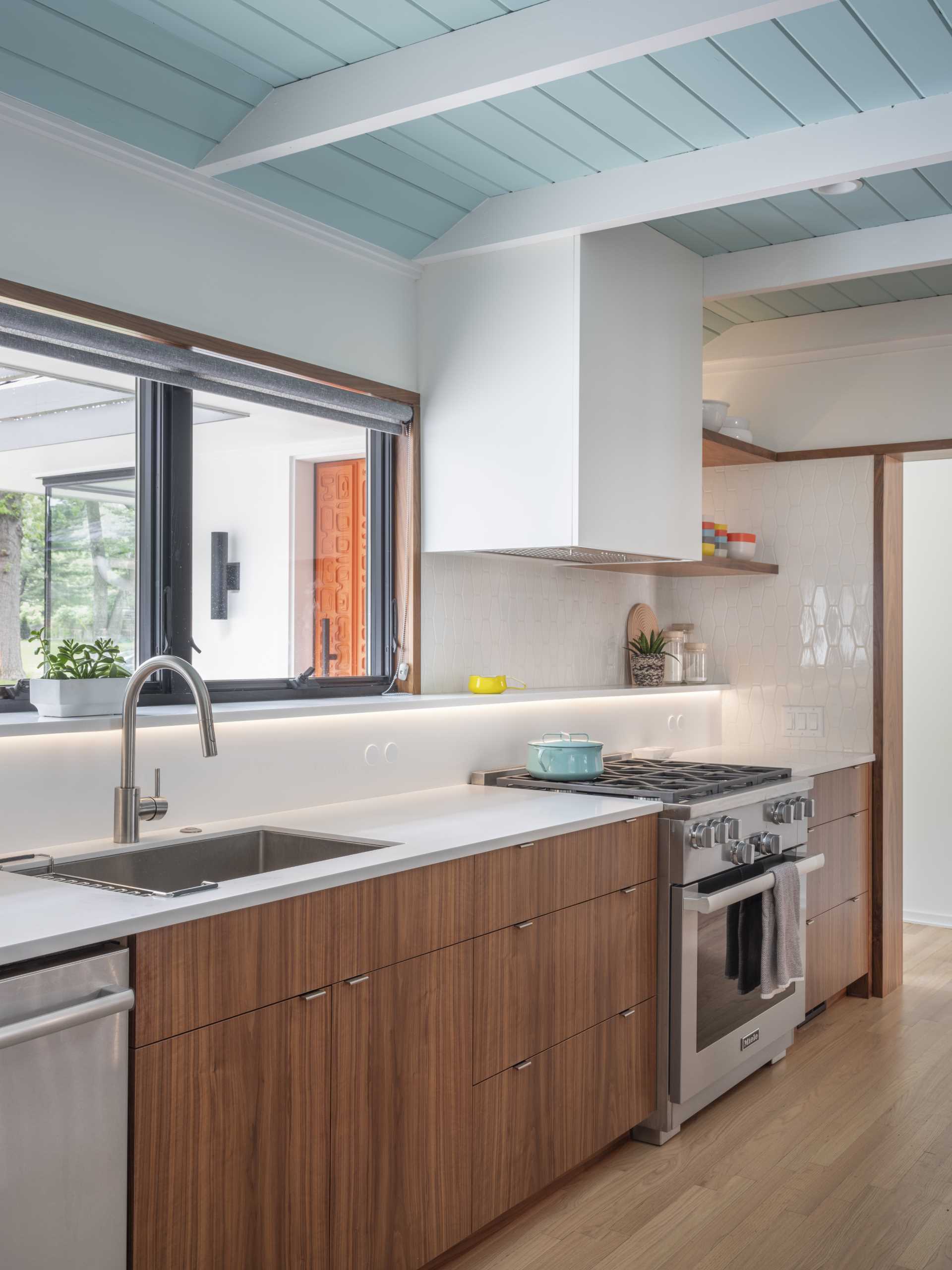 In this updated kitchen, wood cabinetry has been paired with white countertops with matching white tiles, and a light blue ceiling.