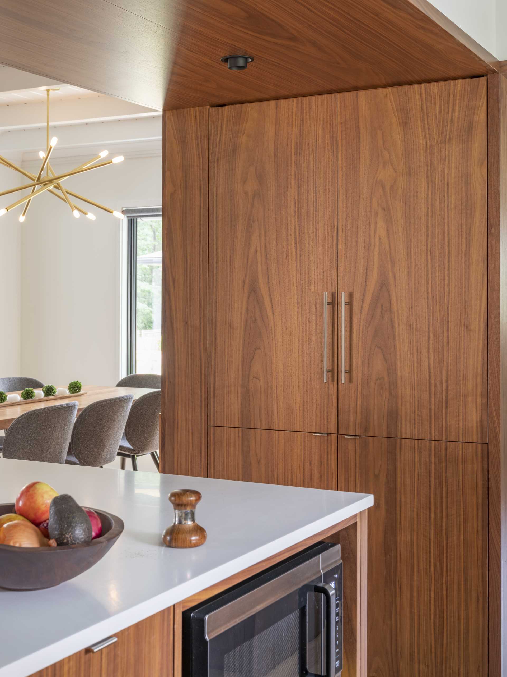 In this updated kitchen, wood cabinetry has been paired with white countertops with matching white tiles, and a light blue ceiling.