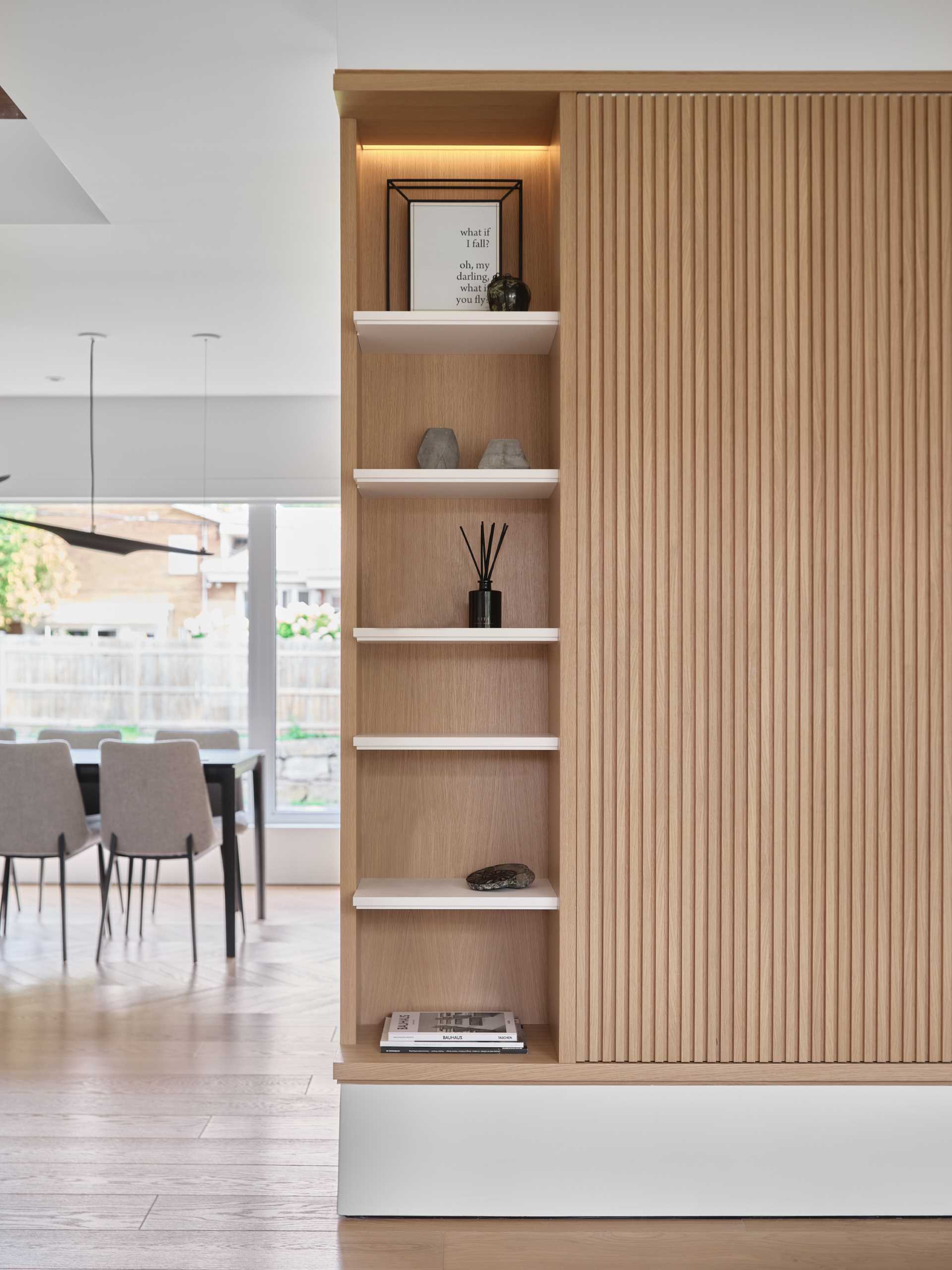 In this modern living room, a wood accent wall is highlighted above the fireplace, while shelving flanks either side of the TV wall, which has a sliding panel to hide the TV.