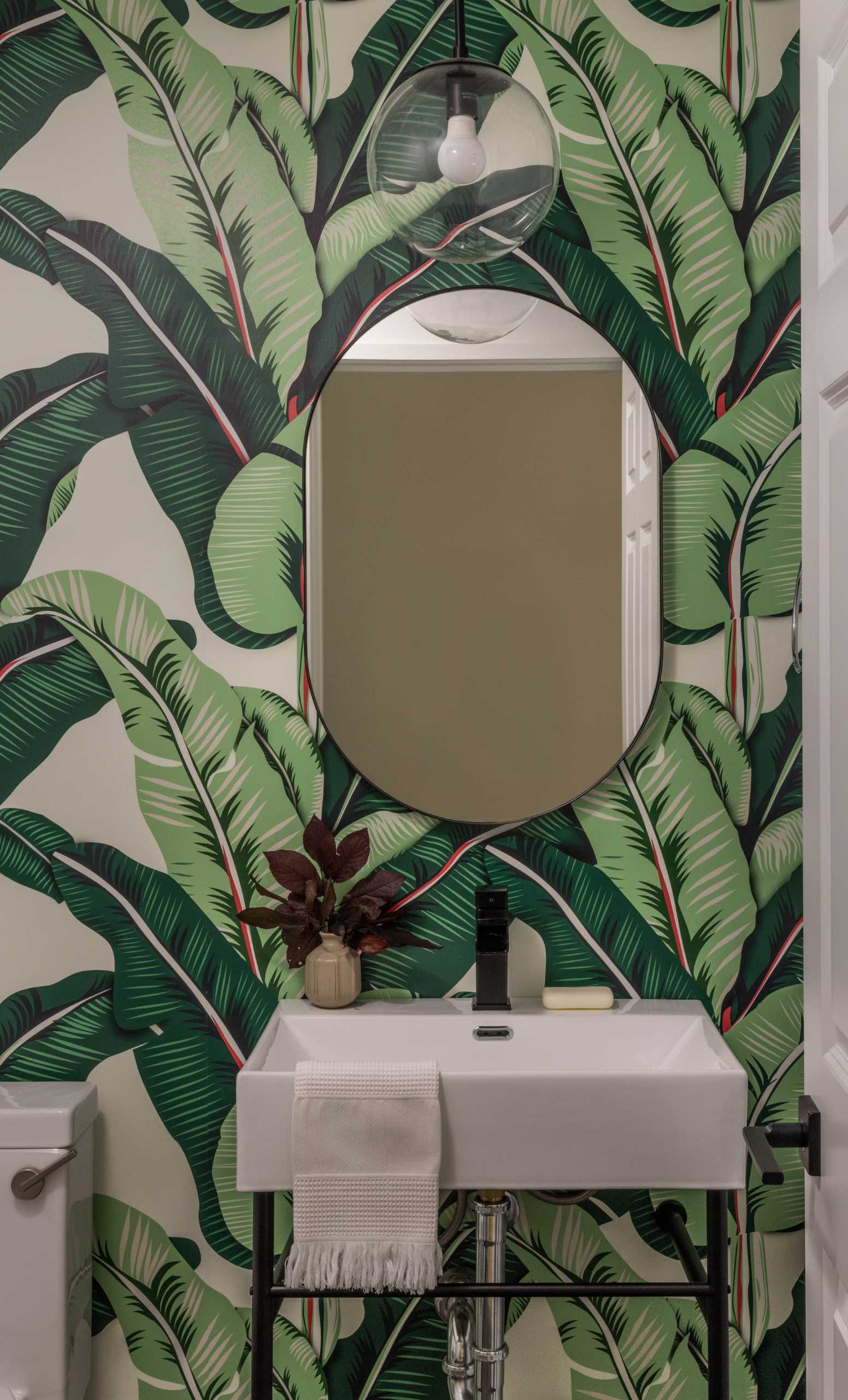 In this powder room, a fun tropical print wallpaper covers the wall adding an unexpected fun element.
