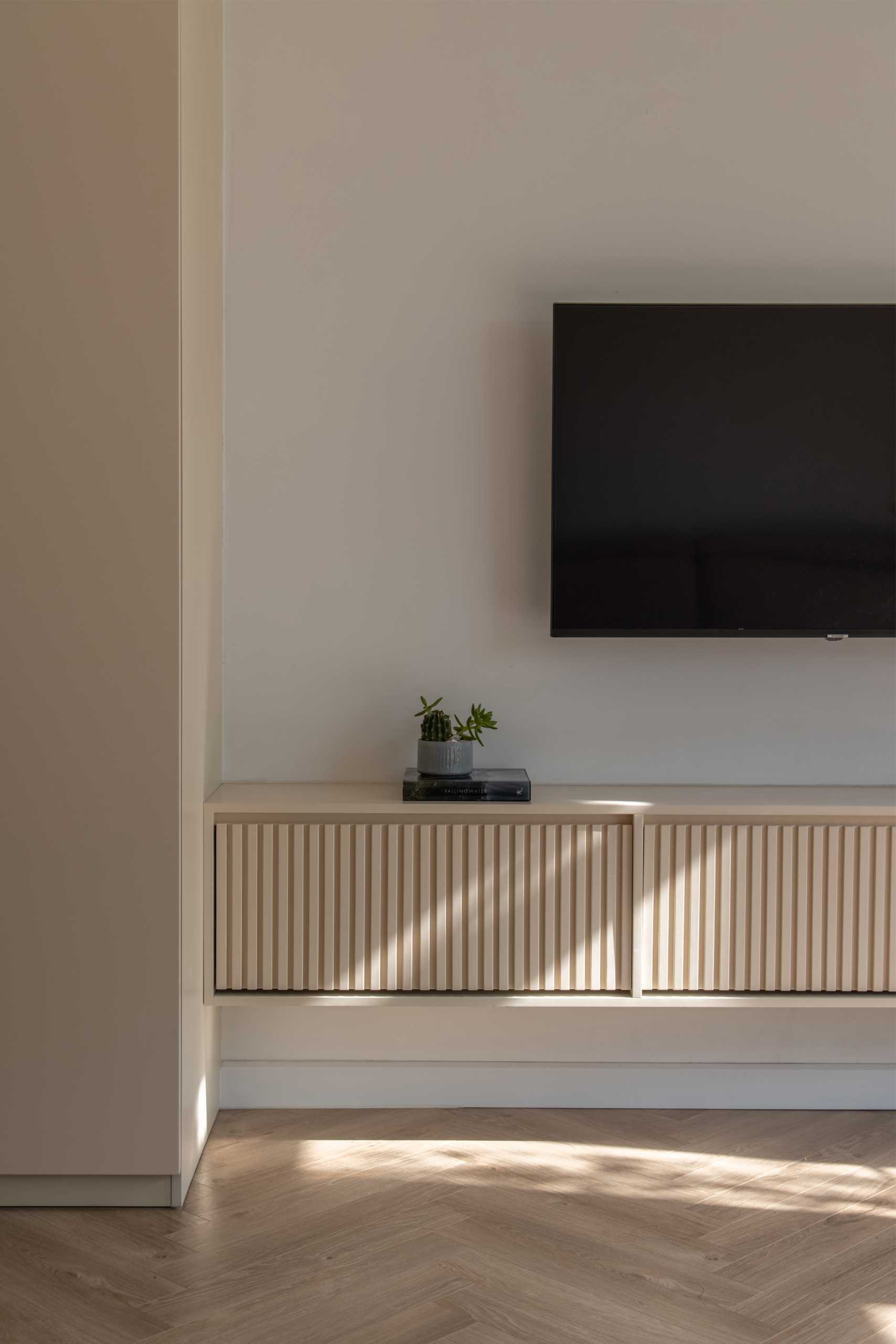 This primary bedroom has a neutral color palette, with floating bedside tables, closets, a dresser, and a vanity area. A sliding door connects the bedroom to a balcony with built-in planters.