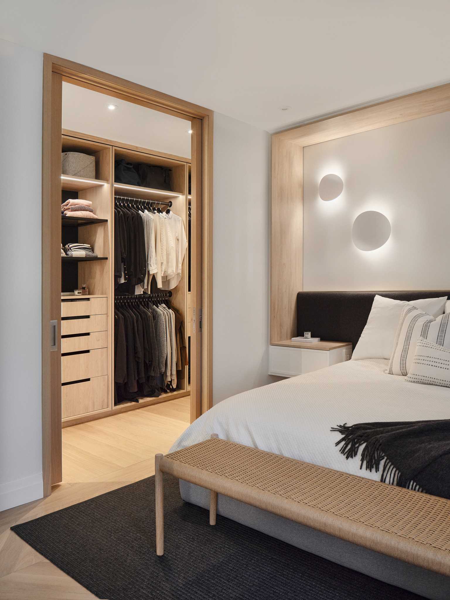 In this primary bedroom, there's a wood detail that wraps around the bed and ends at the bedside tables, while sliding doors open to reveal a custom-designed walk-in closet.
