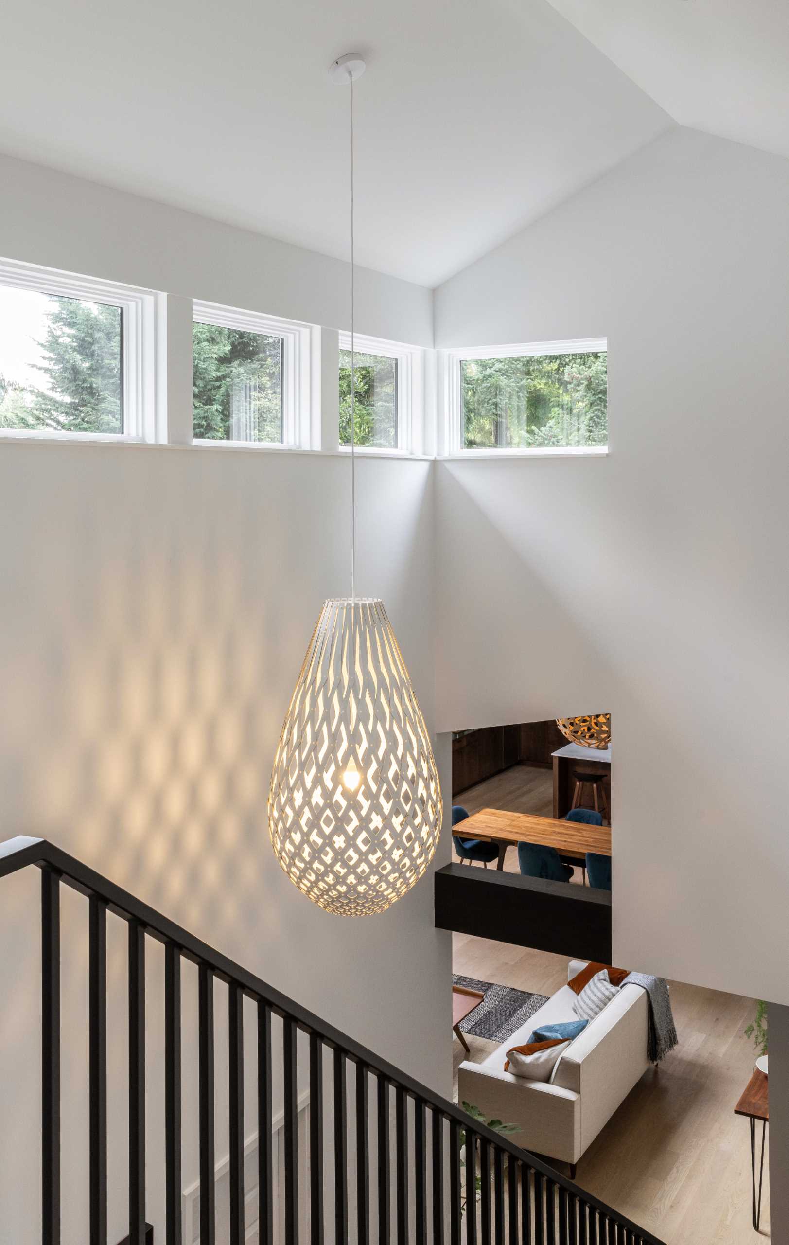 This staircase features a large sculptural pendant light and natural light from a row of windows.