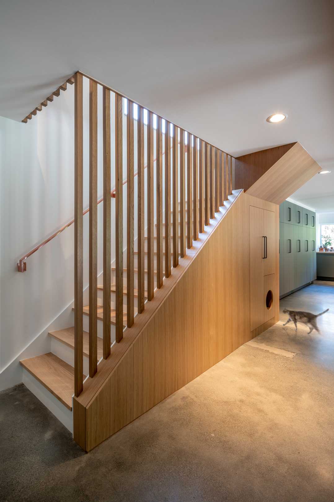 The remodeled basement stairs are now bright and open, with wood slat partitions and cabinetry helping to hide them.