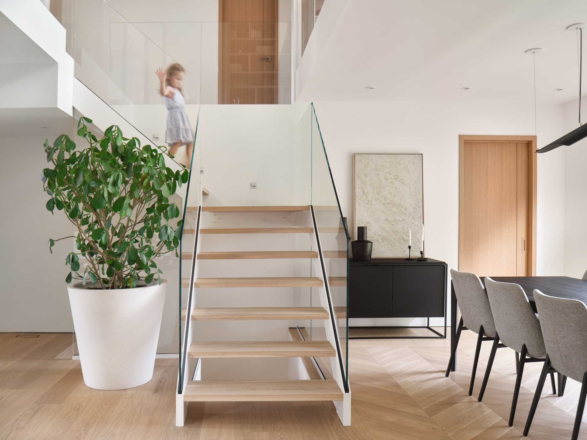 Stairs with wood treads and glass railings lead from the dining area up to the more private spaces of the home.