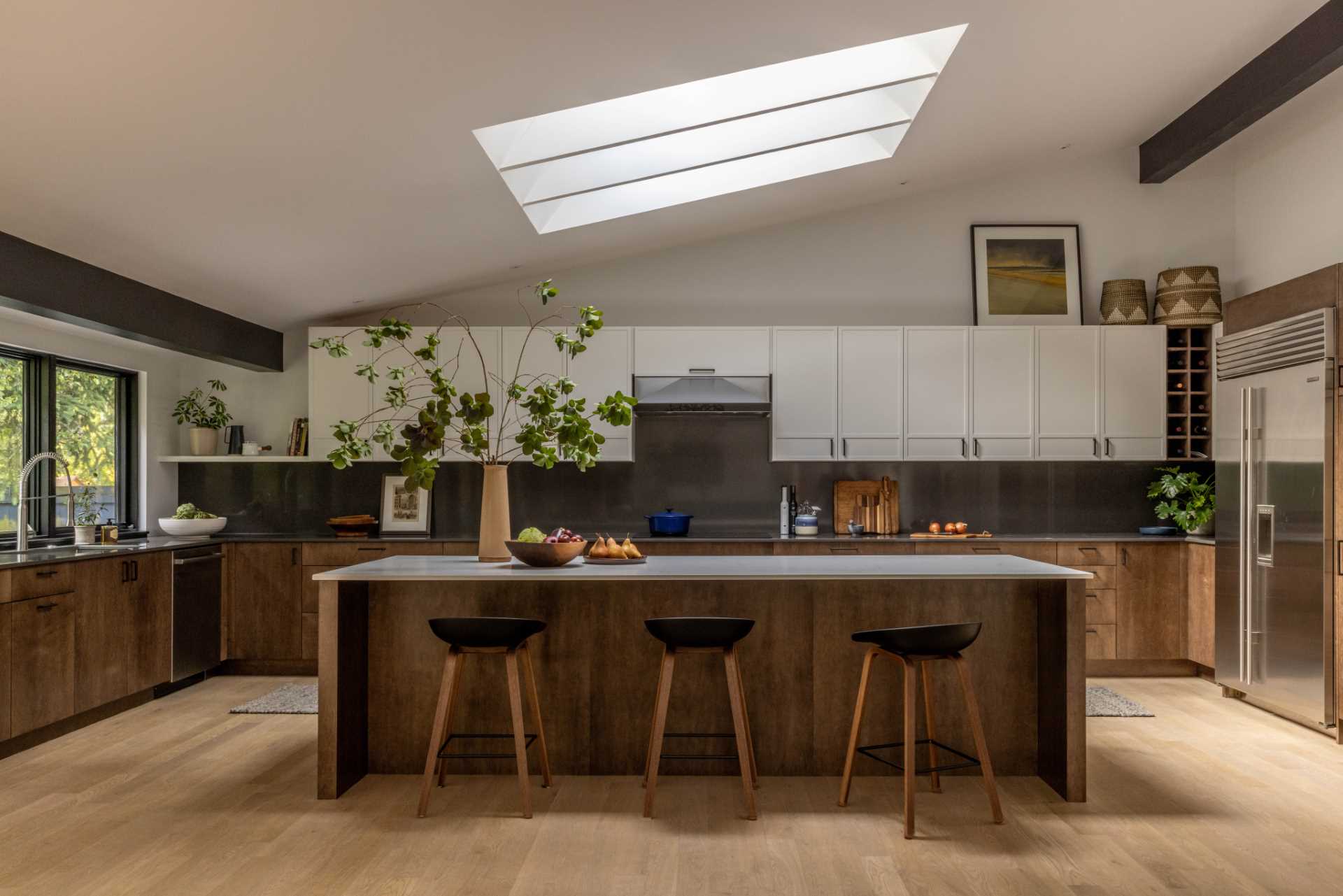 A modern kitchen with wood and white cabinets, black window frames, an island, and a skylight.