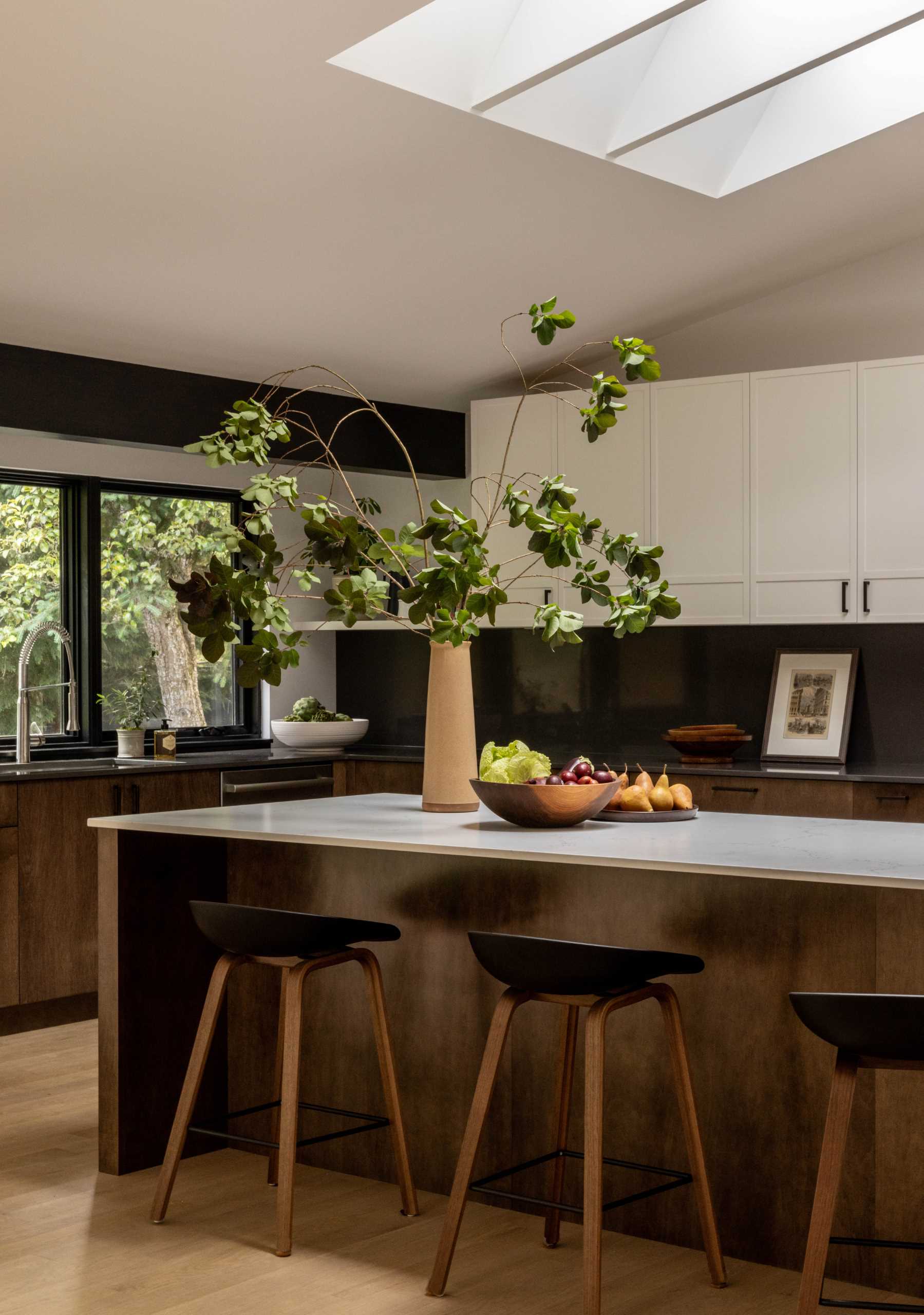 A modern kitchen with wood and white cabinets, black window frames, an island, and a skylight.