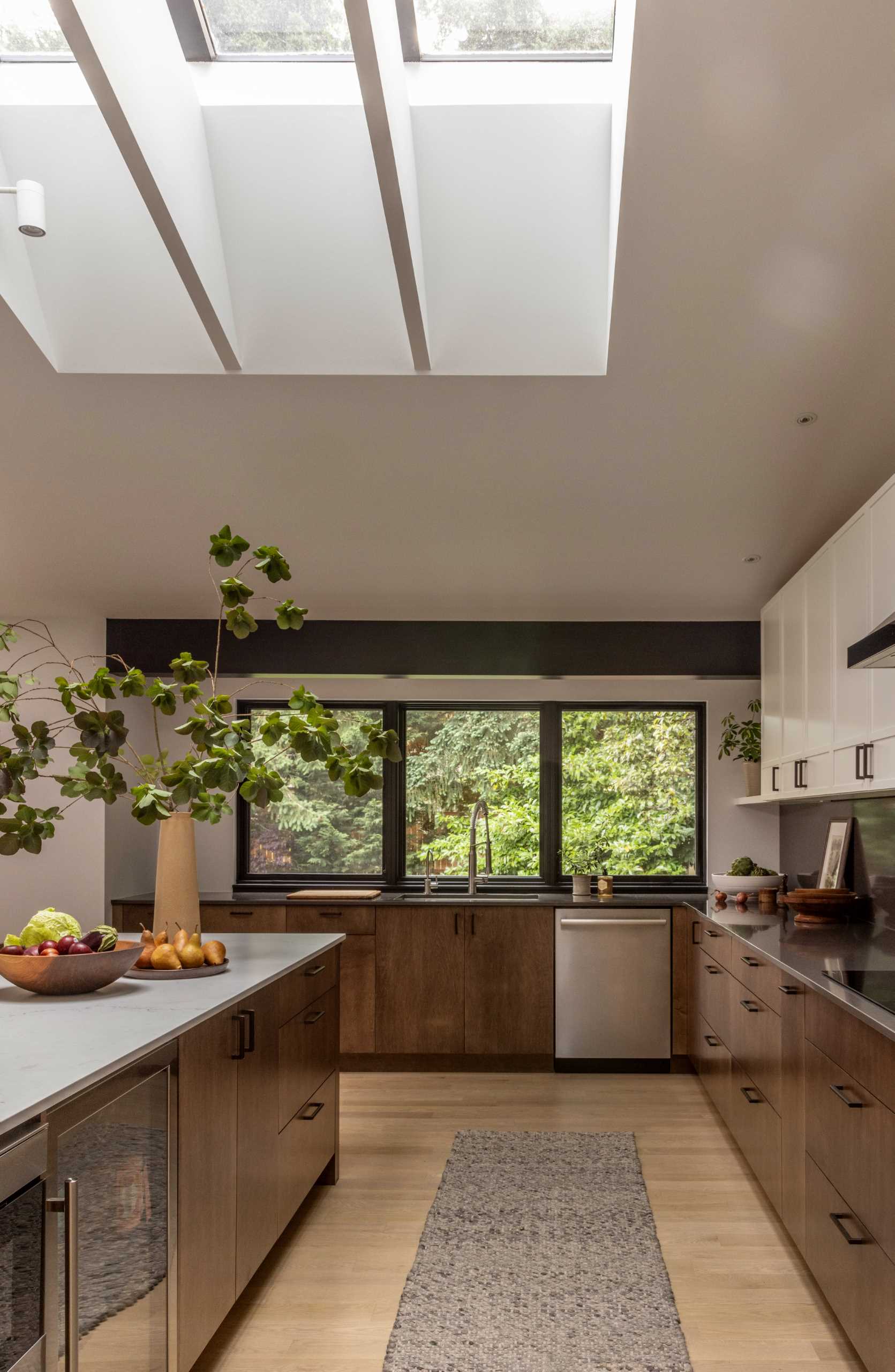 A modern kitchen with wood and white cabinets, black window frames, an island, and a skylight.