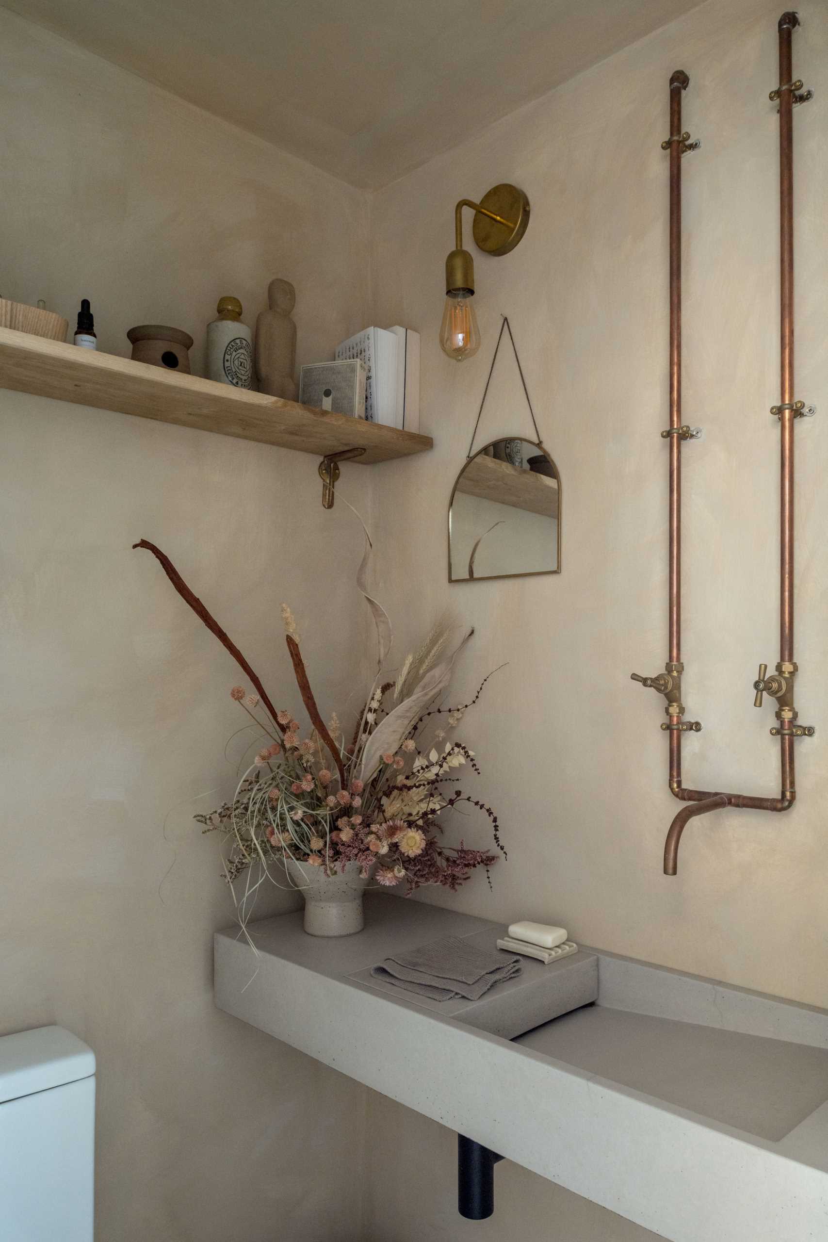 In a powder room, exposed copper pipes become a design element that complements the wall light.