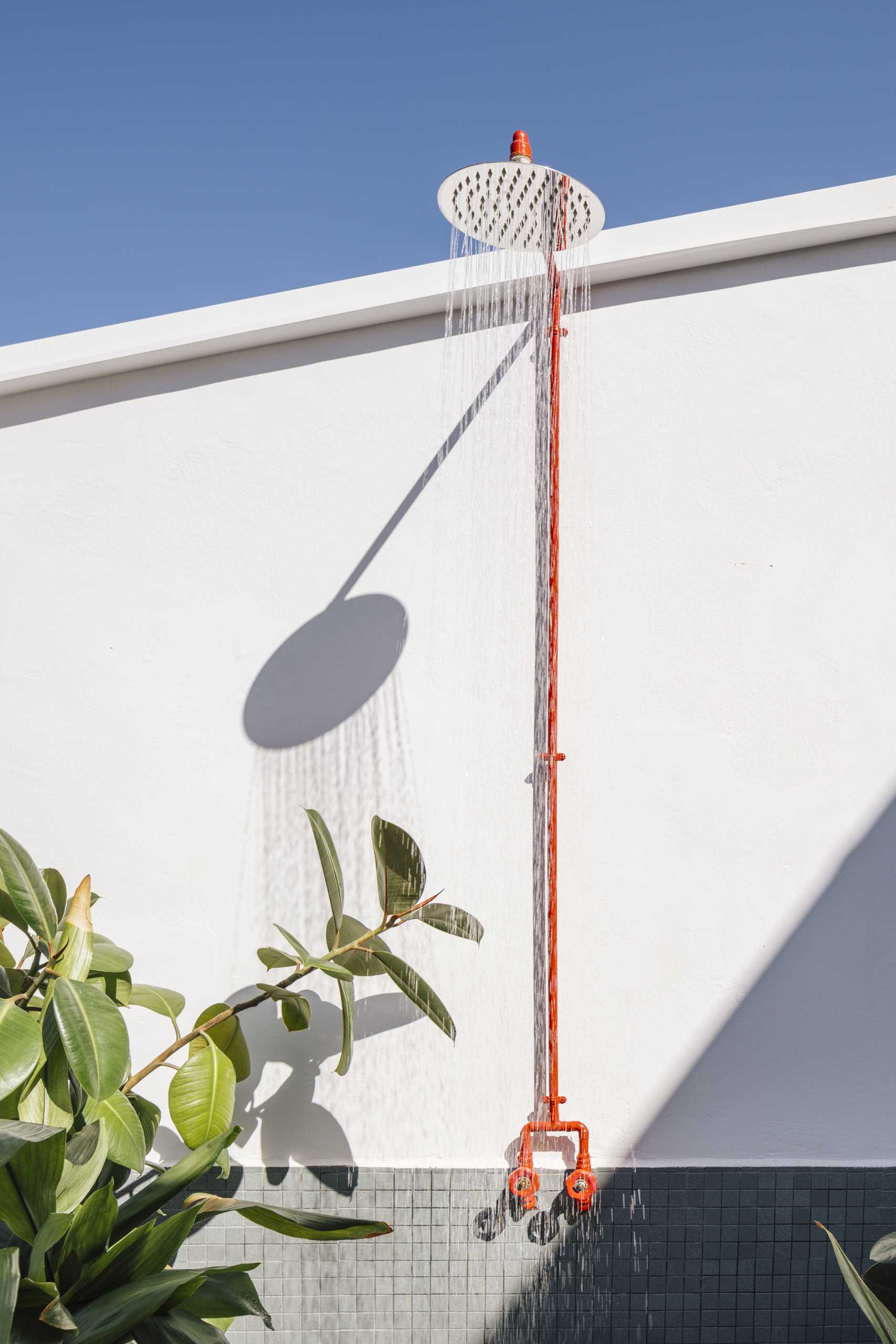 A small apartment with a yellow accent wall has folding doors that open to a small terrace with an outdoor shower, and a daybed that hides an outdoor bathtub underneath.