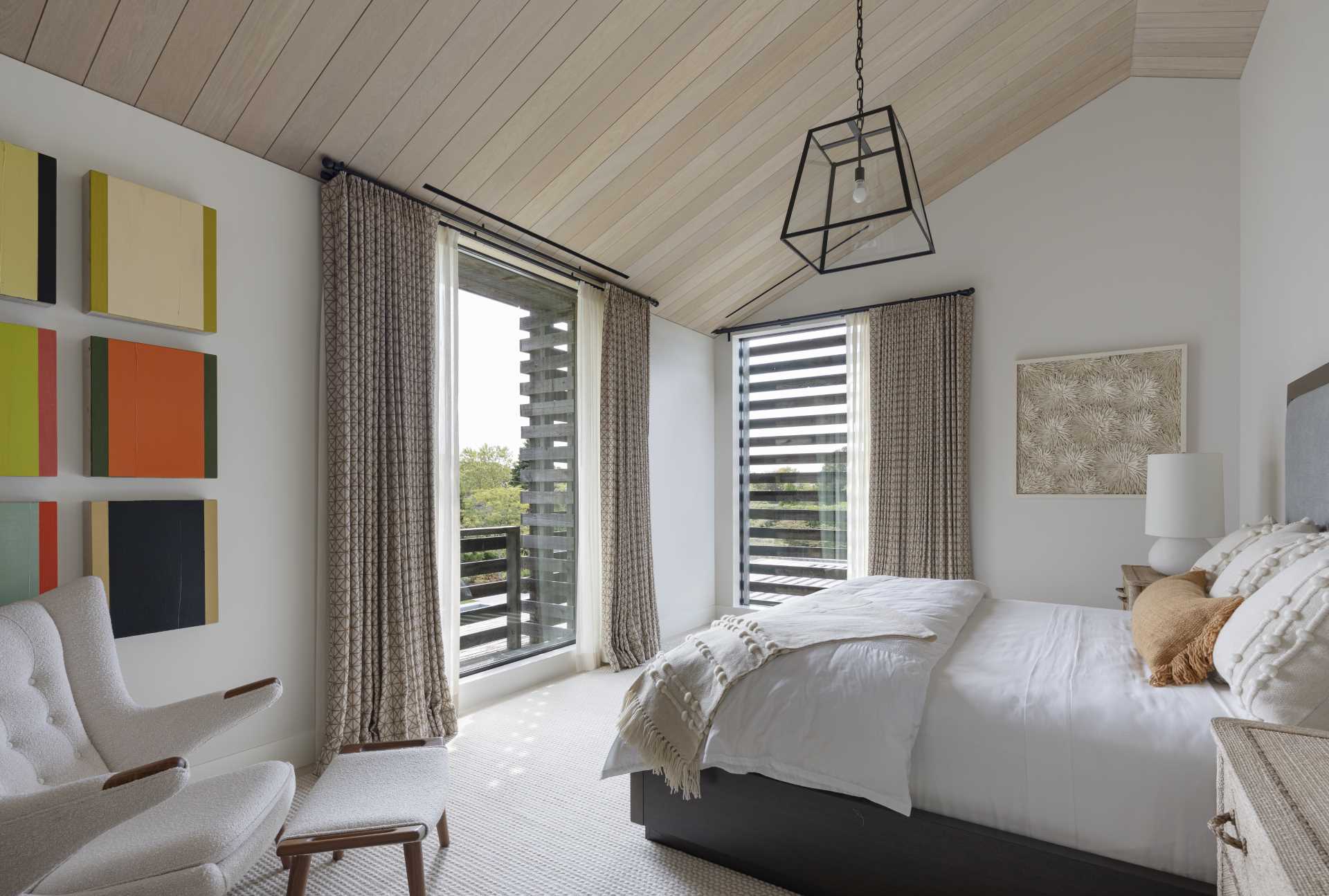 The primary bedroom has a wood ceiling and windows that provide views of the trees.