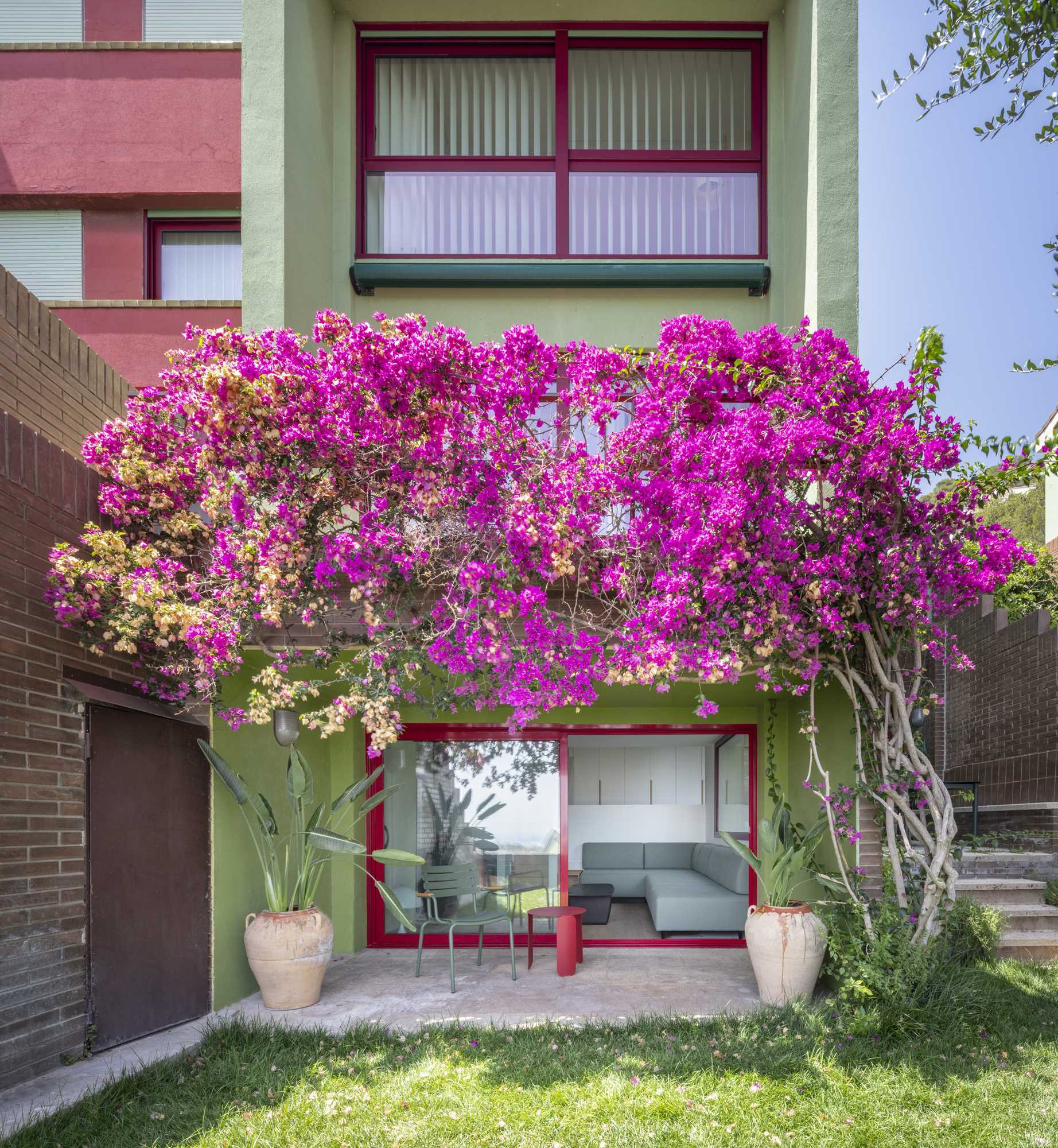 A contemporary home with a green exterior that adorned with colorful flowers.