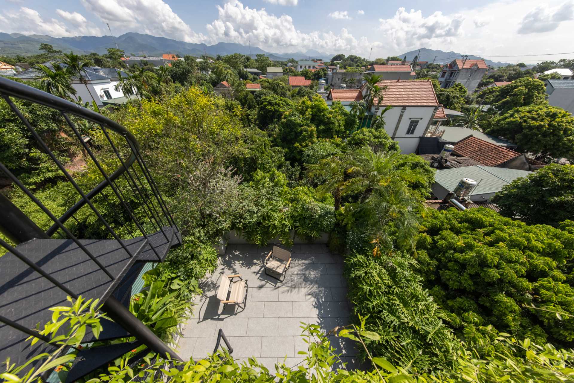 A modern rooftop patio with seating and spiral stairs that lead to an additional rooftop area with a pergola and more plants.