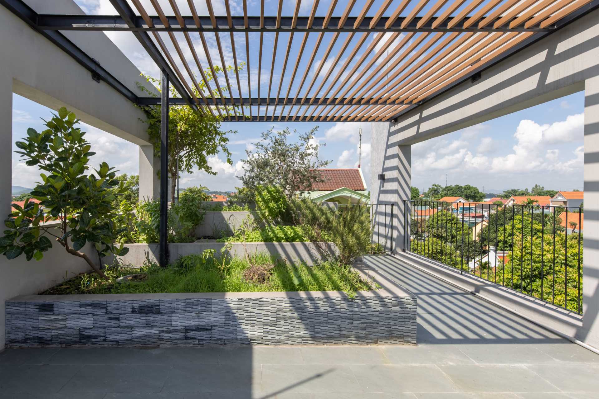 A modern rooftop patio with seating and spiral stairs that lead to an additional rooftop area with a pergola and more plants.