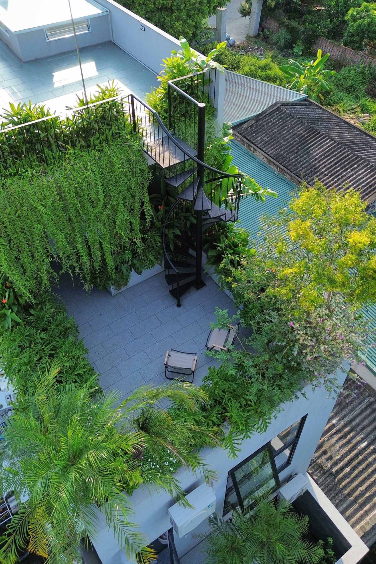 A modern rooftop patio with seating and spiral stairs that lead to an additional rooftop area with a pergola and more plants.