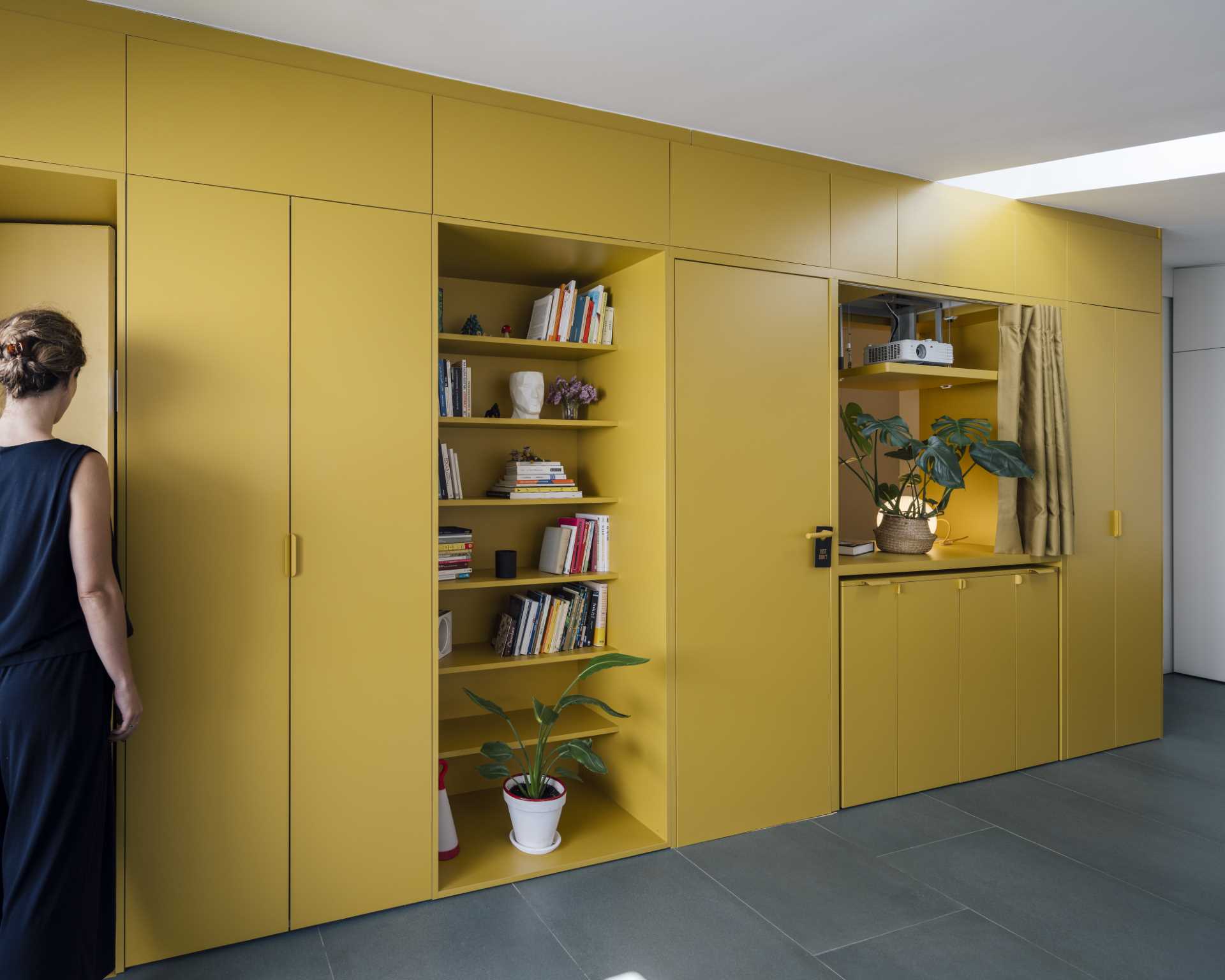 A small apartment with a yellow accent wall that includes plenty of storage and hides the bedroom and bathroom.