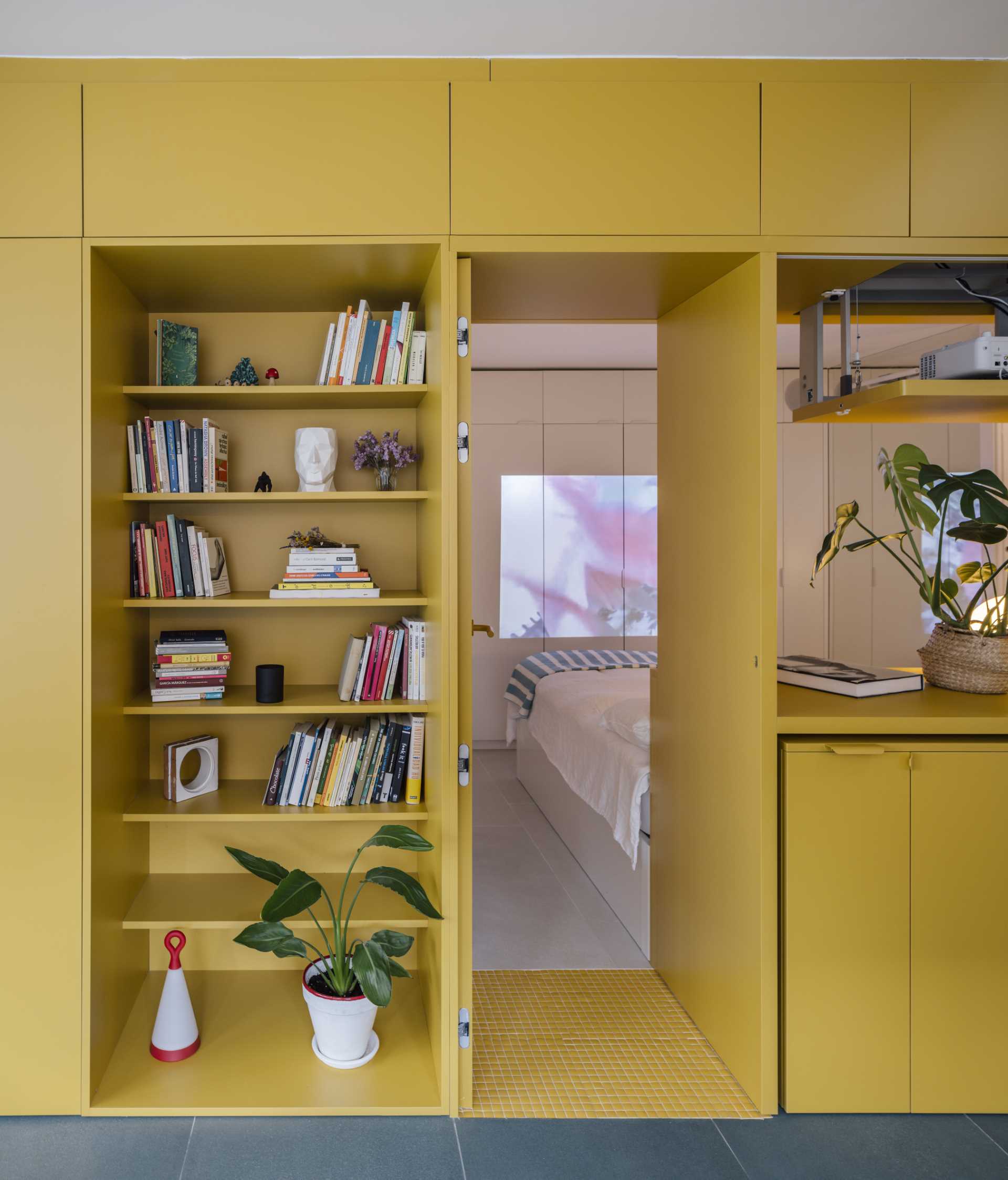 A small apartment with a yellow accent wall that includes plenty of storage and hides the bedroom and bathroom.