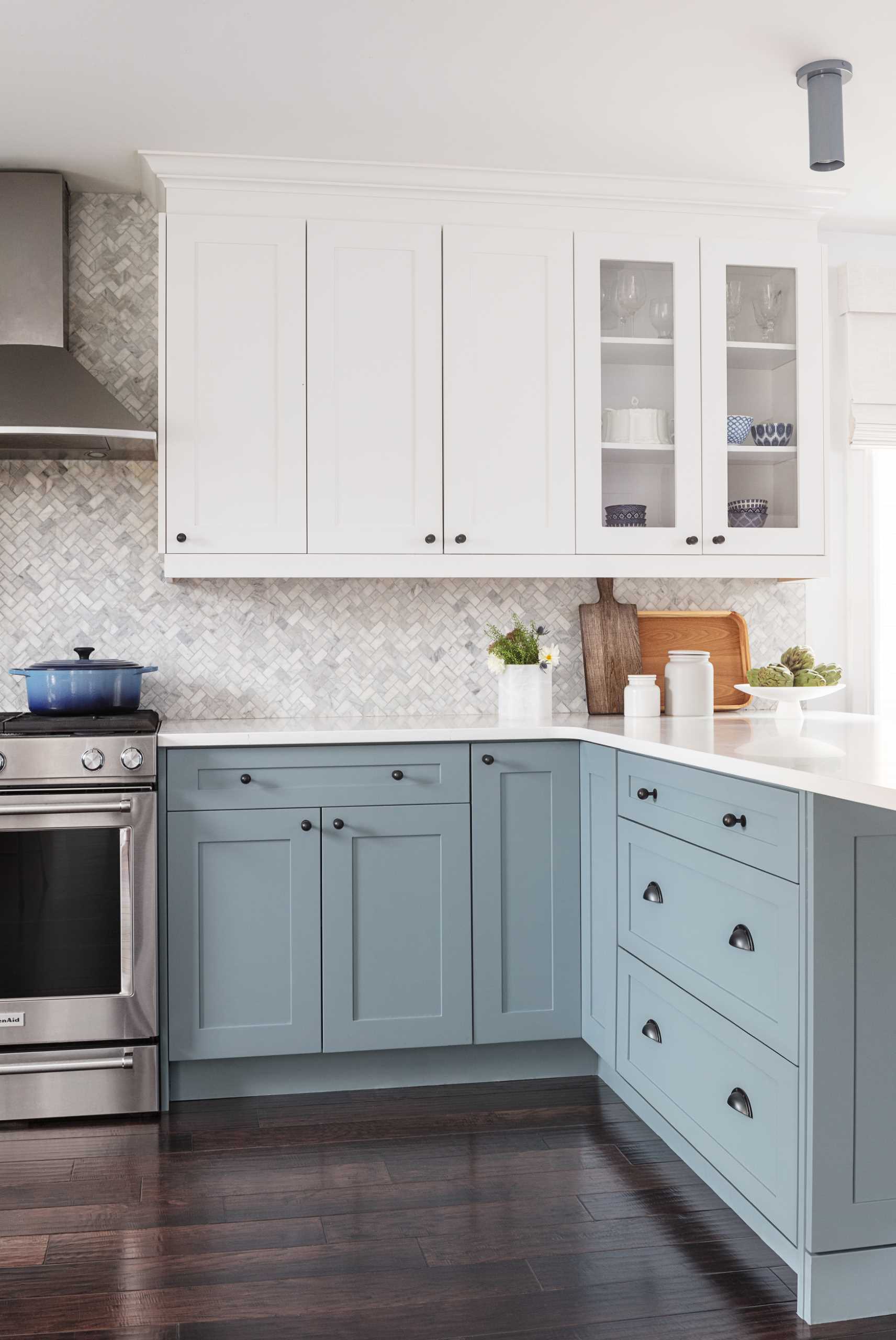 This contemporary kitchen features lower blue cabinets and tile laid in a herringbone pattern acts as a backsplash.