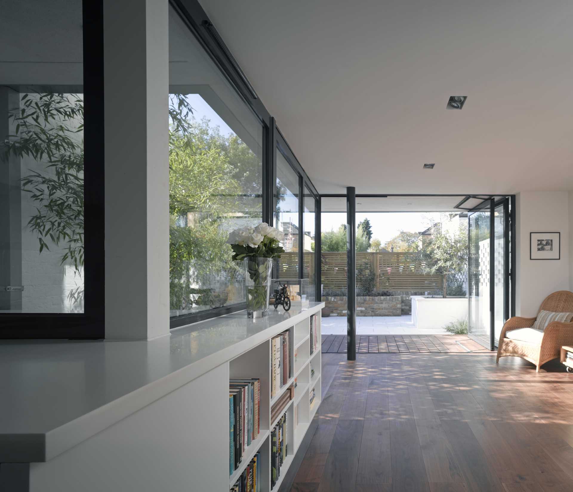 A garden room, which is filled with natural light, includes a white bookshelf under the window.