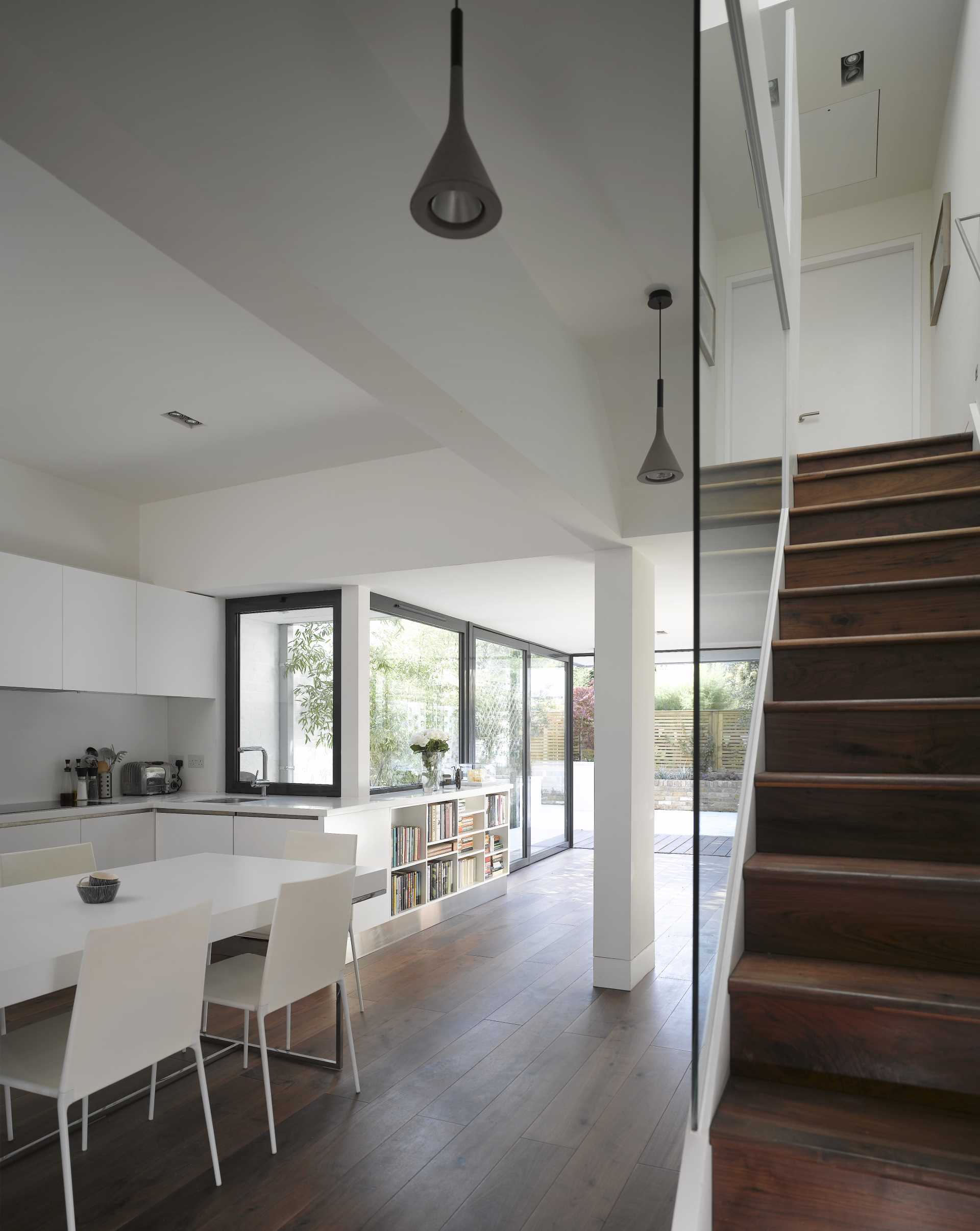 The bookshelf meets the kitchen cabinets, which have a minimalist appearance and a matte white finish.