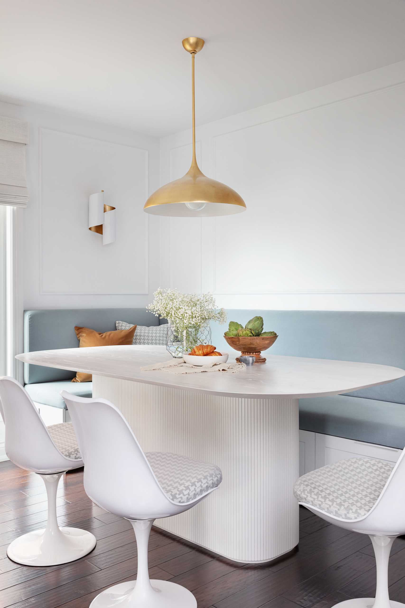 A contemporary dining area with banquette seating that lines the corner. The pale blue cushions add a soft pop of color to the mostly white space.