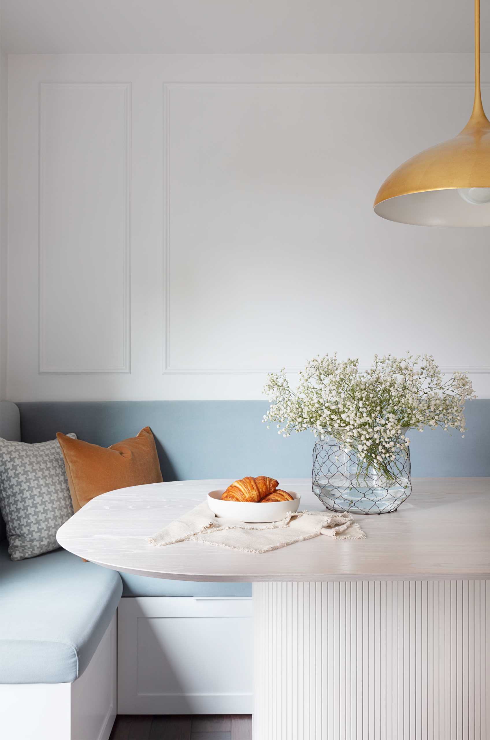 A contemporary dining area with banquette seating that lines the corner. The pale blue cushions add a soft pop of color to the mostly white space.