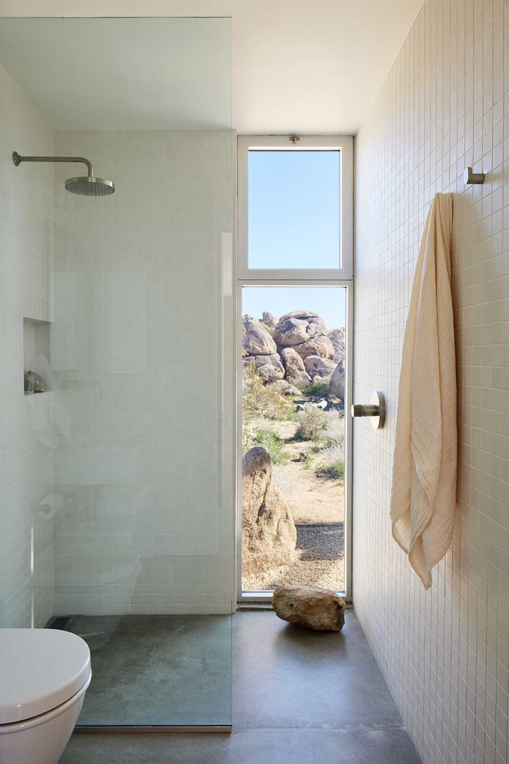 In the bathroom, tiles cover the walls, while a tall vertical window perfectly frames the view.