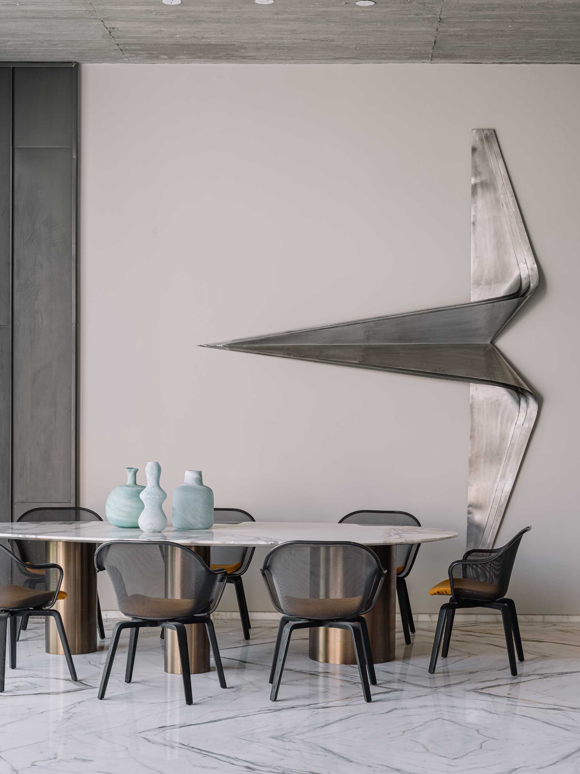 A modern dining room with a high ceiling and a metal sculpture on the wall.